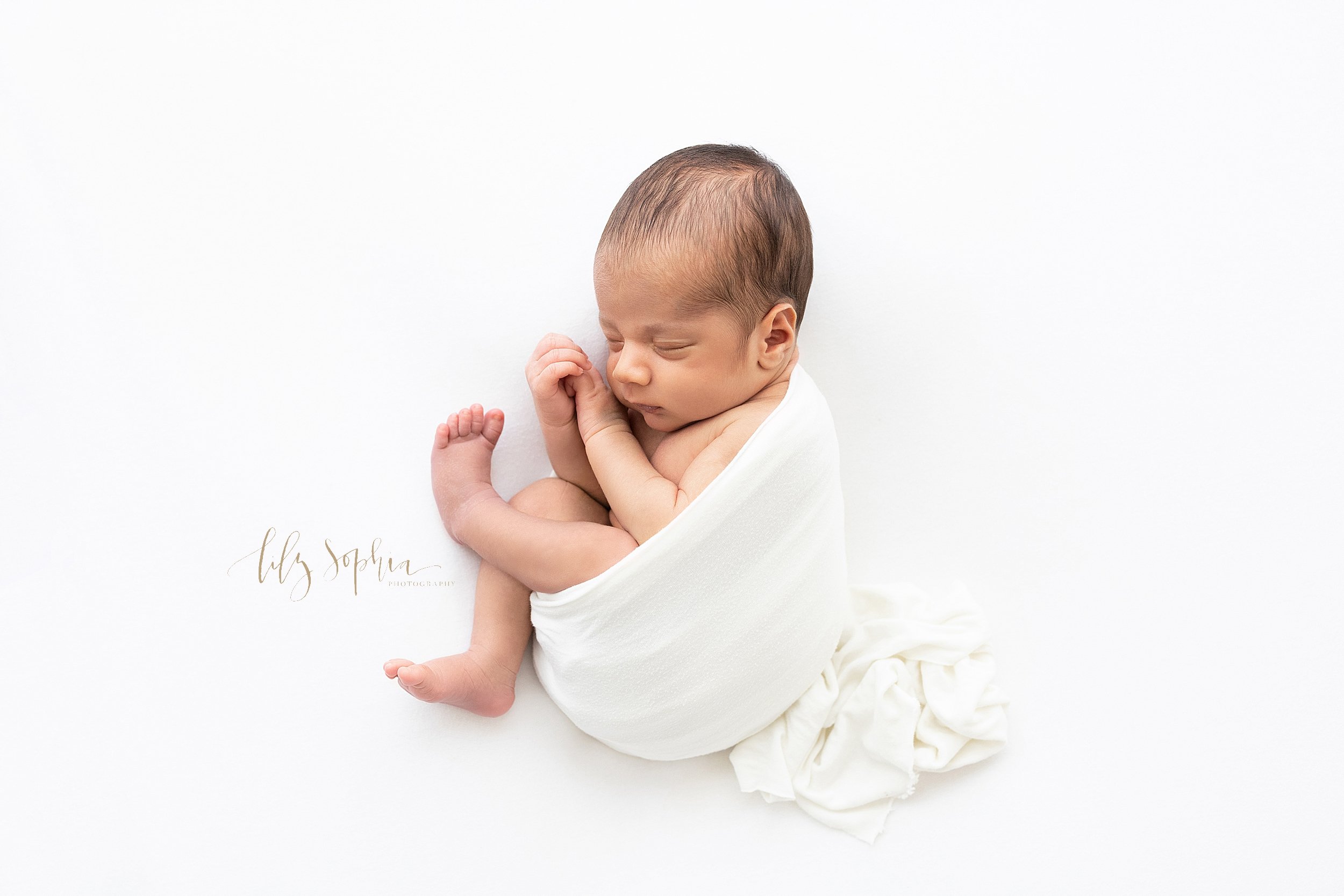  Newborn portrait of a peacefully sleeping baby boy cradled in a stretchy swaddle as he lies on his side taken in a studio near Midtown in Atlanta that uses natural light. 