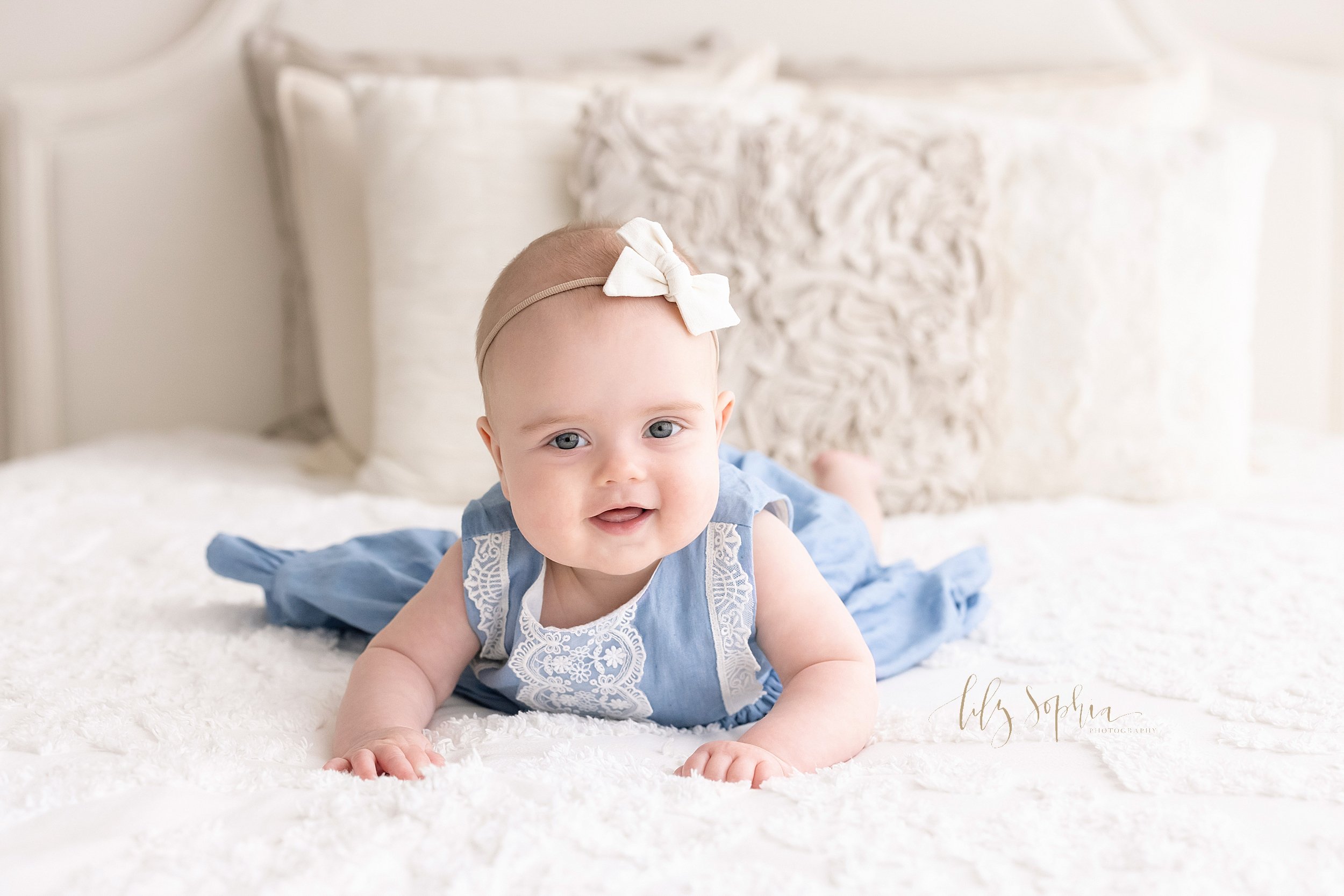  Baby photo shoot of a six month old girl lying on her stomach and pushing herself up on a bed taken in a studio in Ponce City Market in Atlanta, Georgia that uses natural light.  