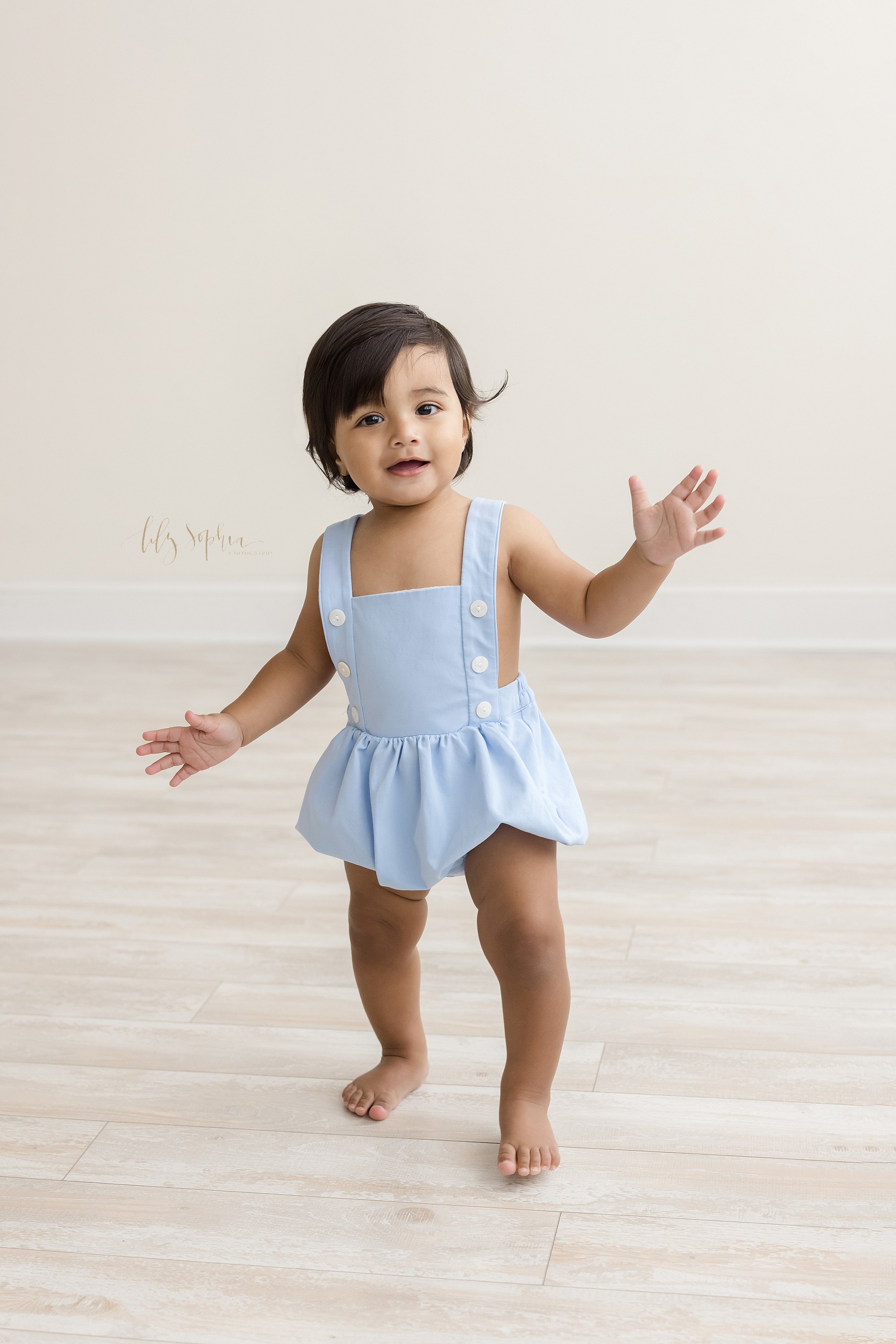  First birthday photo session with a one year old boy as he waves hello and toddles across the floor of a studio that uses natural light located near Virginia Highlands in Atlanta. 