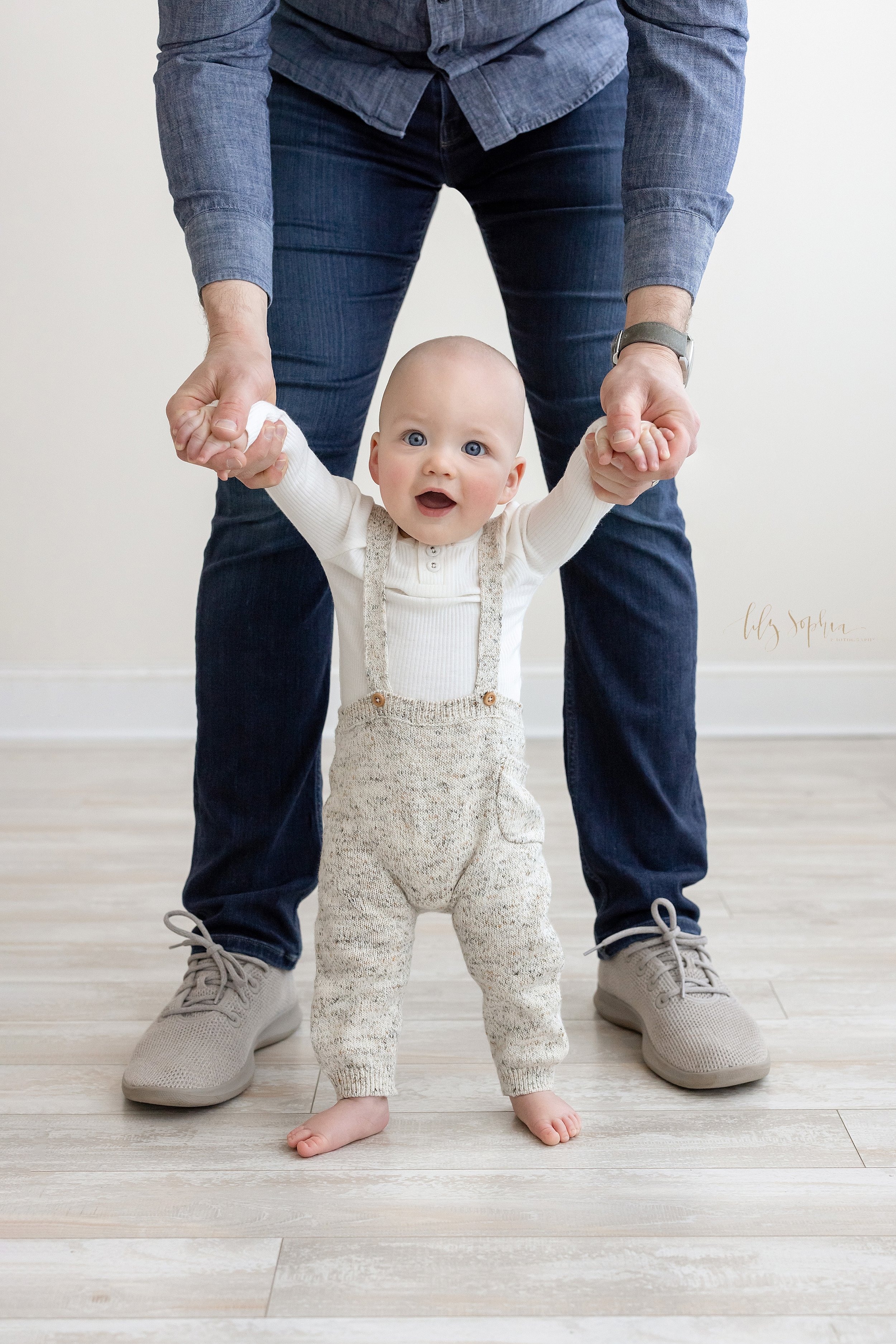  Milestone photo of an eight month old baby boy as his father holds his hands, so he can walk in front taken in a natural light studio near Midtown in Atlanta, Georgia. 