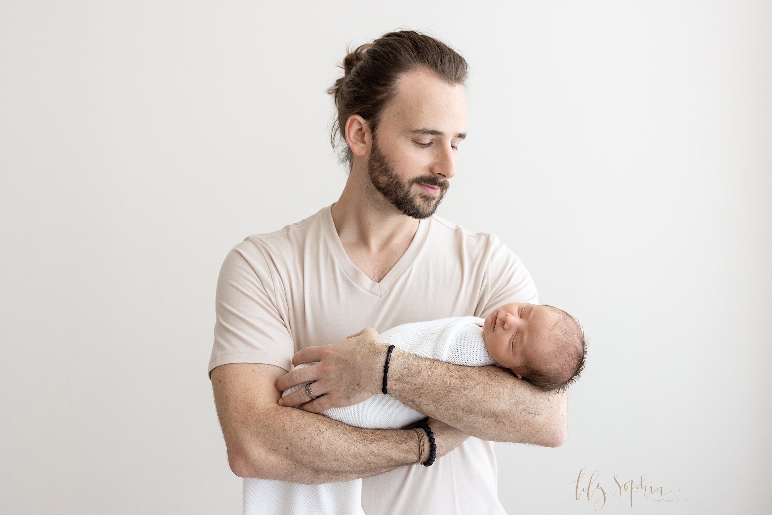  Newborn picture of a father cradling his newborn baby boy in his arms as he marvels at him as the infant sleeps taken in a natural light studio near Ansley Park in Atlanta. 