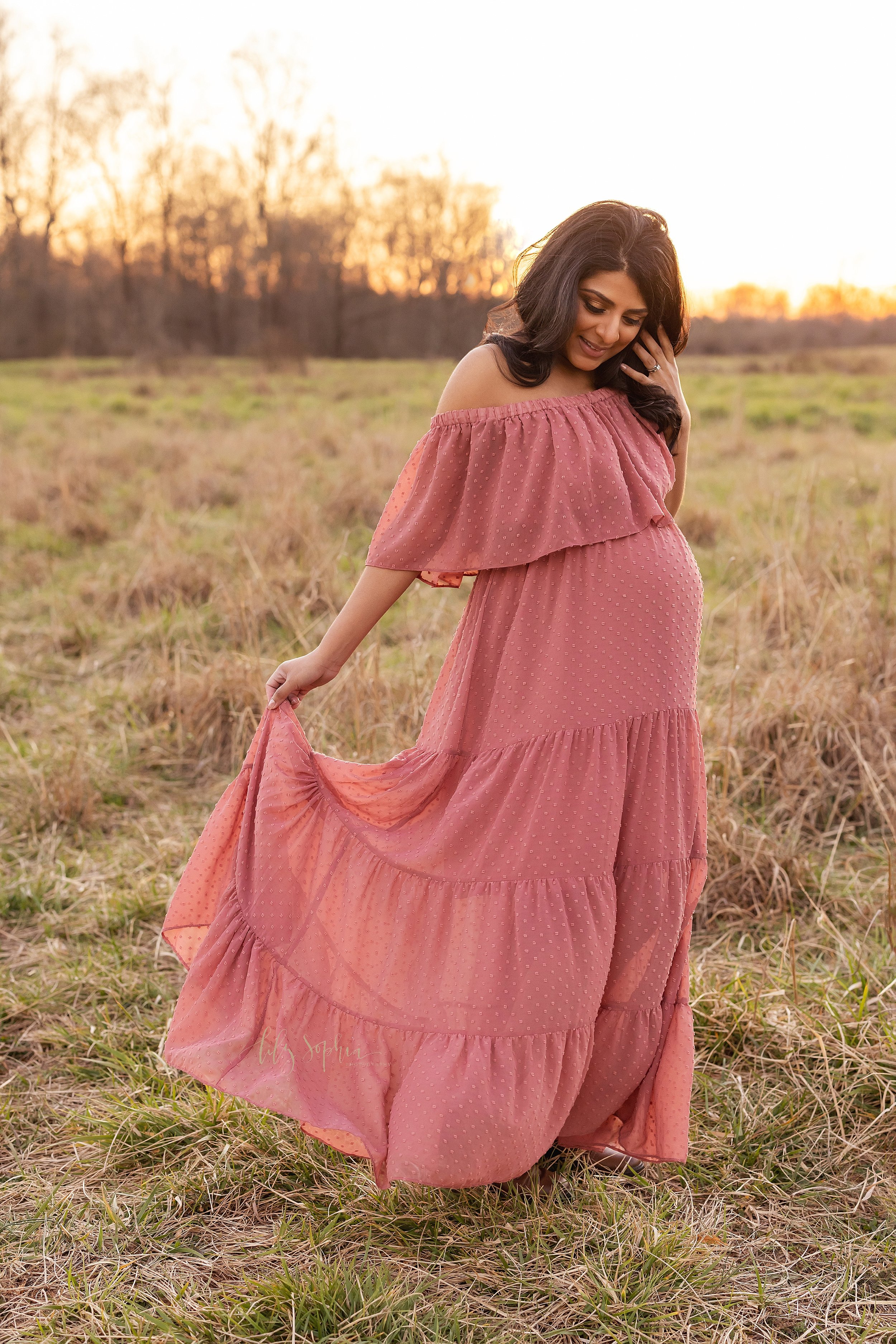  Maternity photo session with a pregnant mother wearing a rose off the shoulder full length ruffled gown with a wide ruffle bodice standing in a field near Atlanta, Georgia at sunset. 