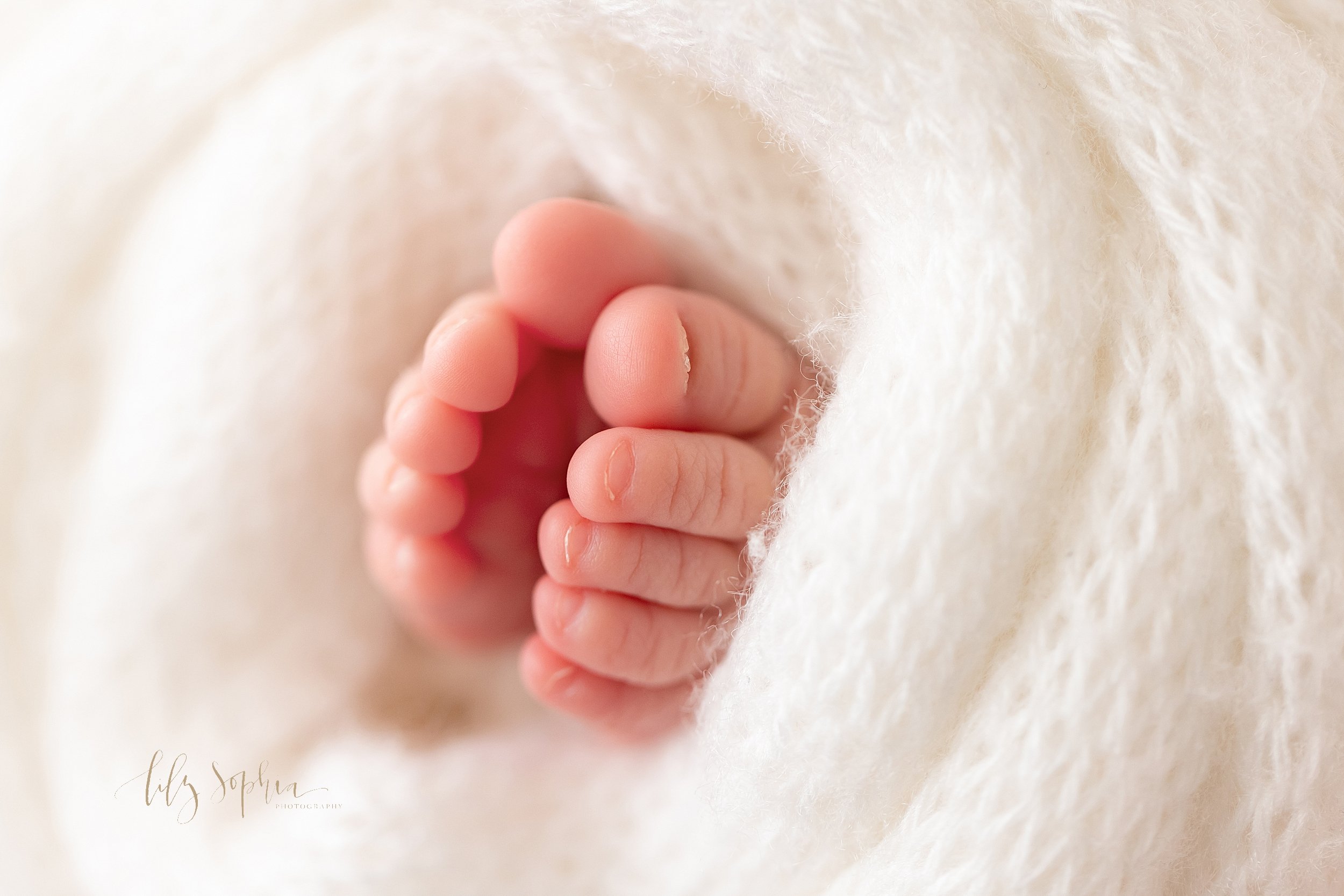  Close-up photograph of the tiny toes of a newborn baby peeking out from a soft white blanket taken near Oakhurst in Atlanta in a natural light studio. 