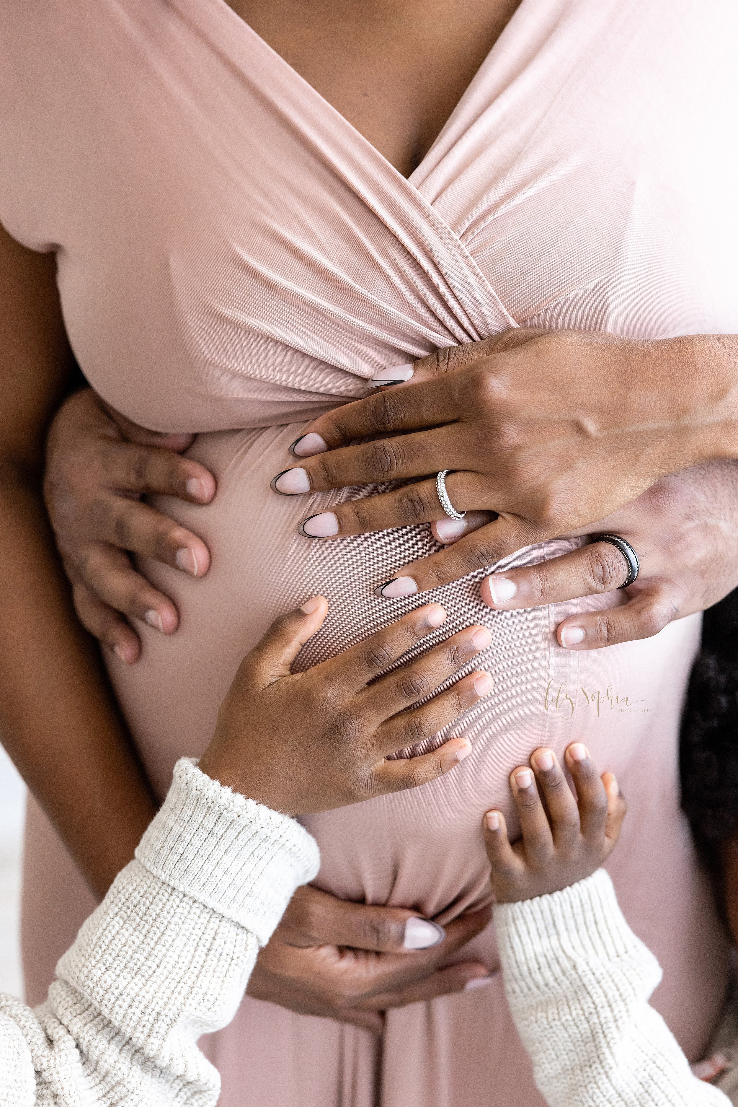  Maternity family portrait of an African-American mother’s belly with the hands of the family touching the child in utero taken in a studio near Old Fourth Ward in Atlanta that uses natural lighting. 