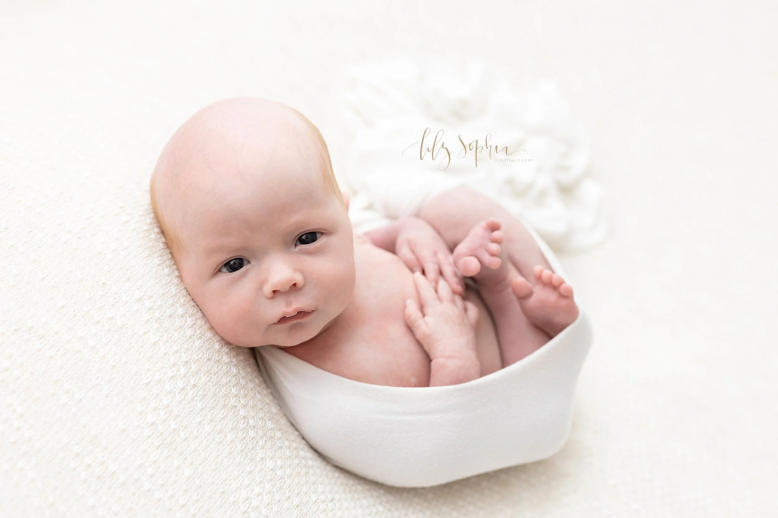  Newborn portrait of a wide awake infant boy as he lies on his back cradled in a stretchy swaddle taken in a natural light studio near Virginia Highlands in Atlanta. 