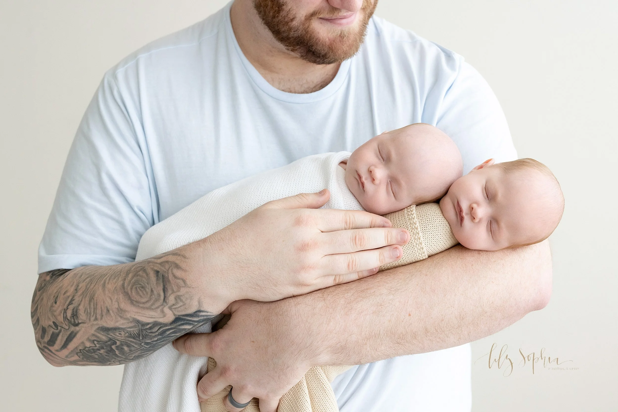  Newborn twin portrait of a father holding both of his infant sons in his arms as he stands in a natural light studio near Kirkwood in Atlanta, Georgia. 