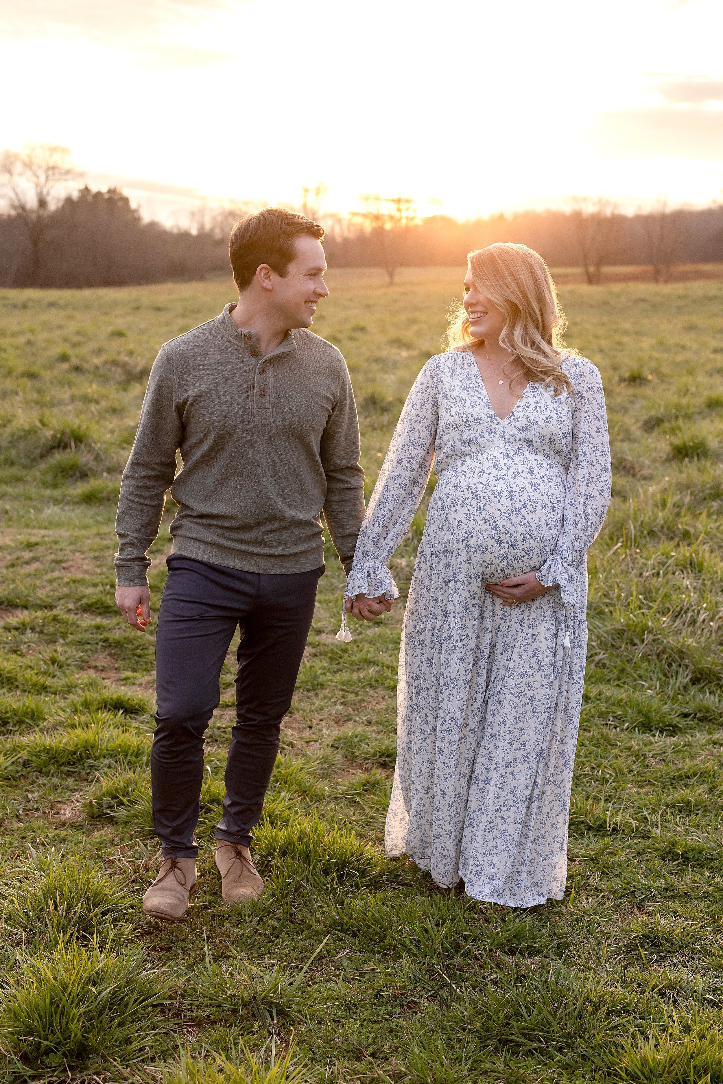  Maternity photo session in an Atlanta field of an expectant couple as they walk hand in hand and talk to one another taken at sunset. 