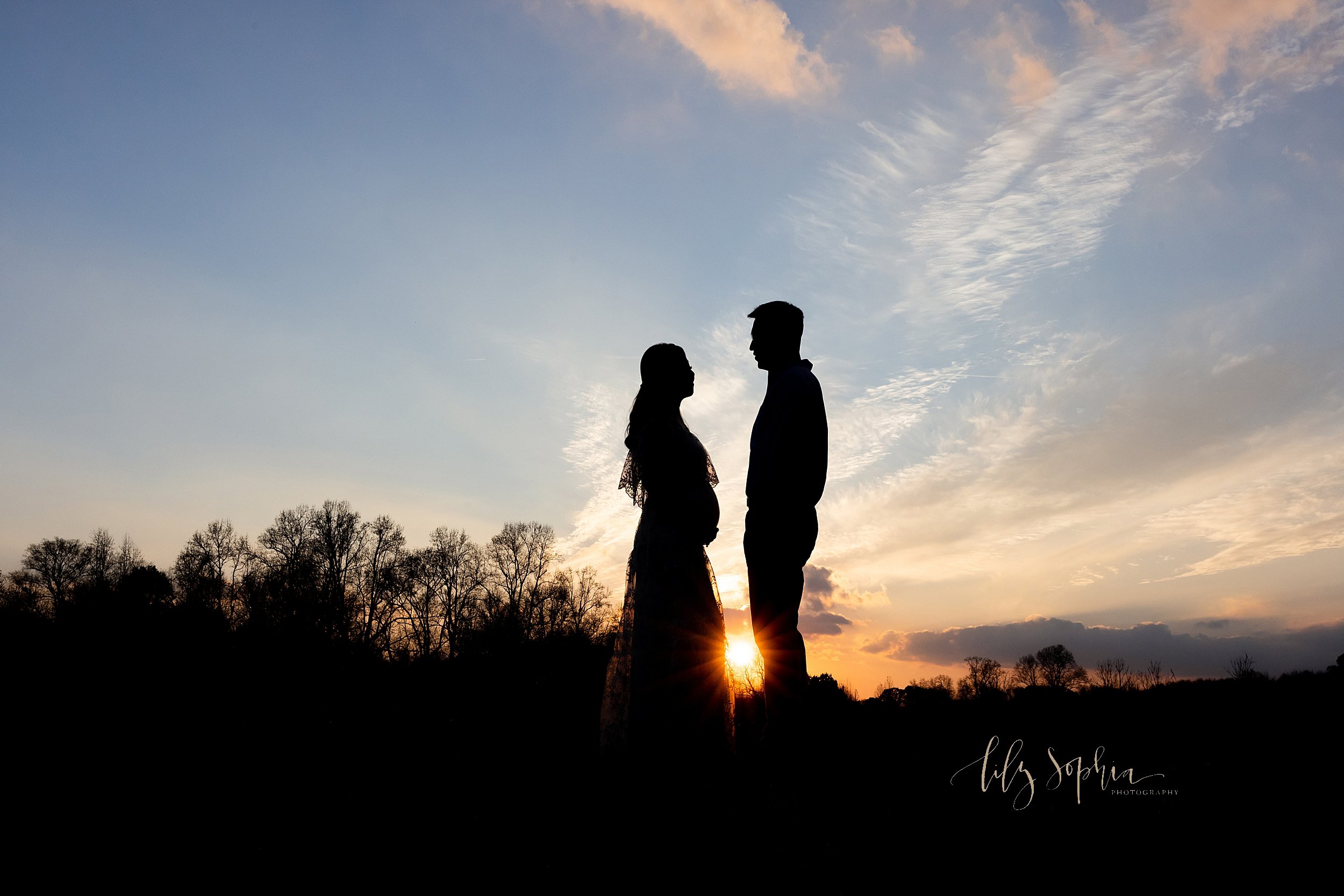  Maternity photograph taken at sunset as the couple face one another atop a grassy knoll in a field near Atlanta, Georgia highlighting their profile silhouettes. 