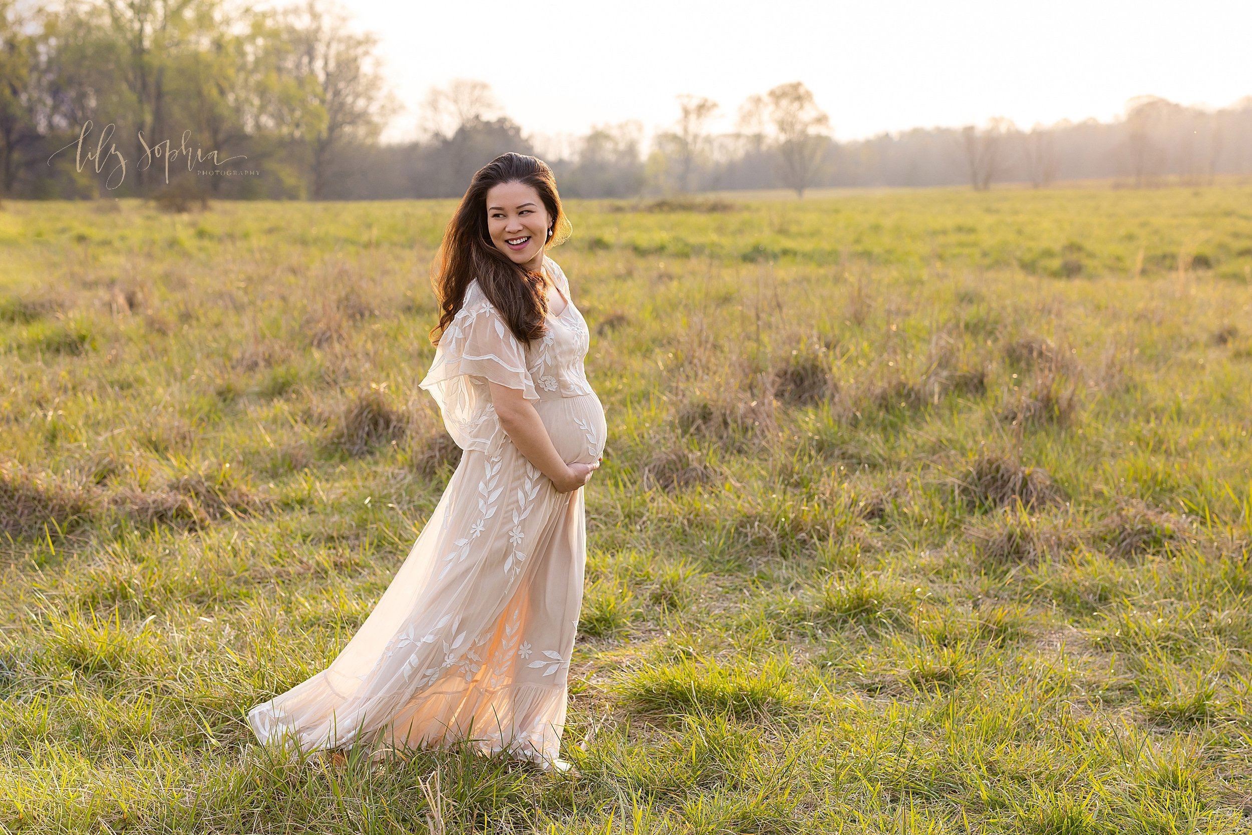  Maternity portrait of a radiant expectant mother as she walks in an Atlanta field holding her belly at sunset as she turns her head to look over her right shoulder. 