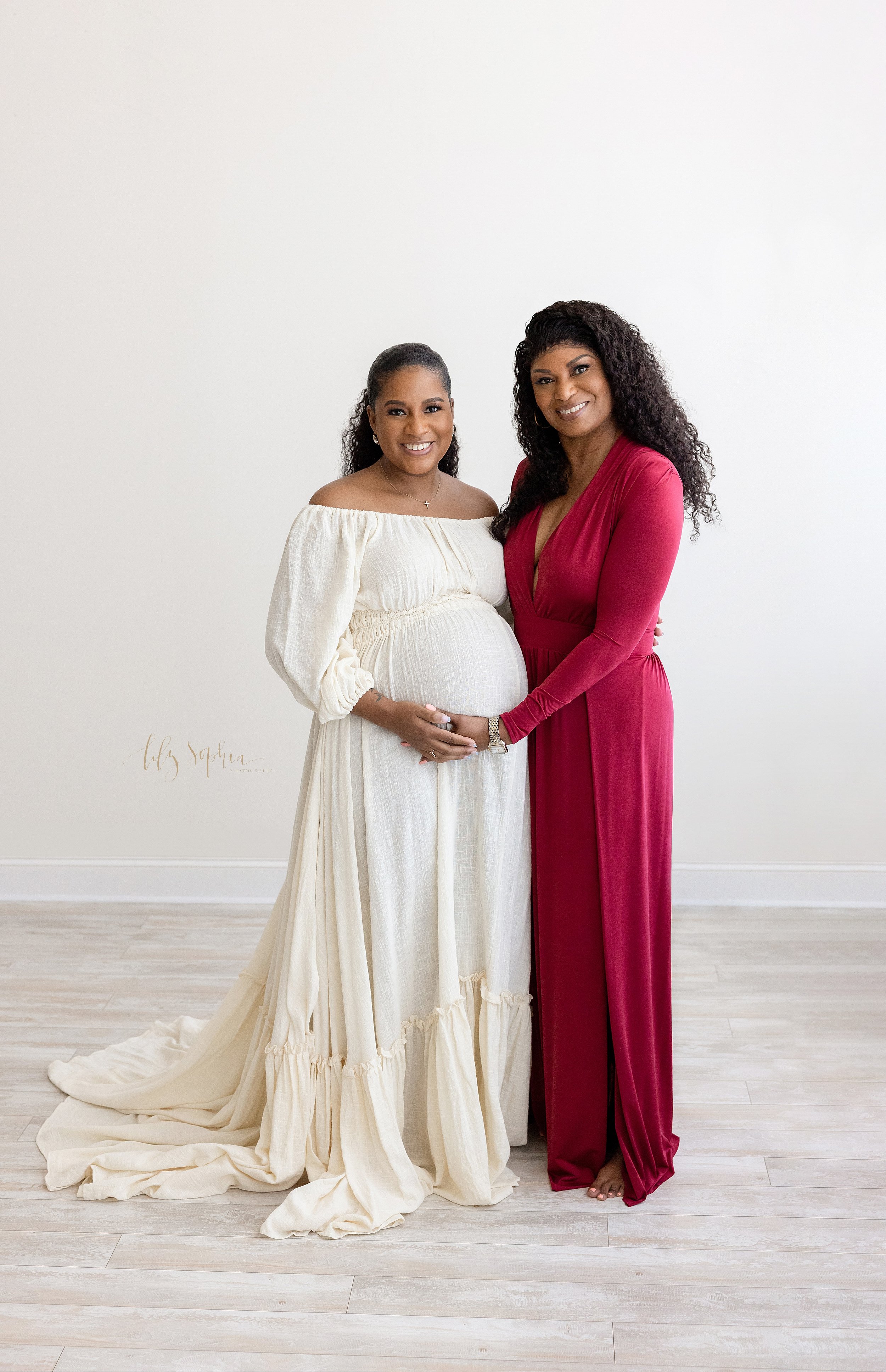  Black maternity photo session with an African-American expectant mother standing next to her mother as the grandmother places her hand on her daughter’s belly and her daughter places her hand on her mother’s hand taken in a studio near Midtown in At