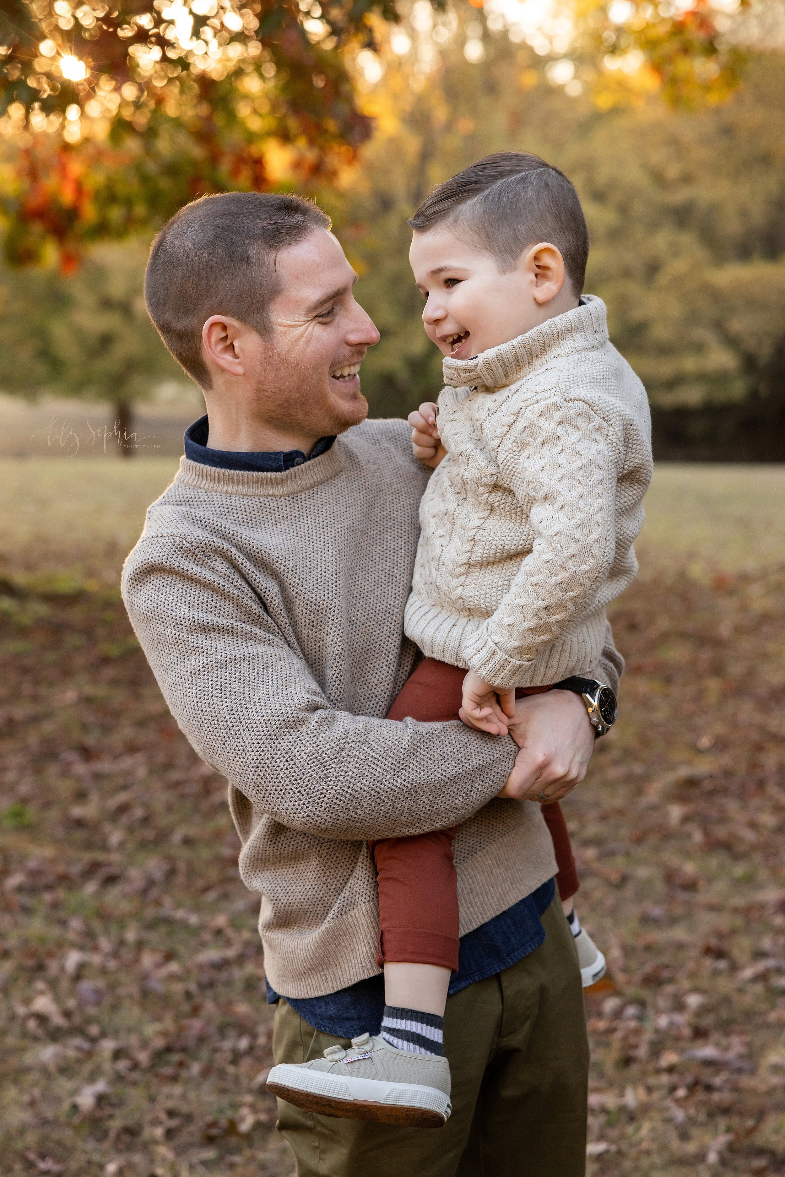  Family photo of a father holding his young son in his arms during autumn as the two of them talk with one another taken at sunset in a park near Atlanta, Georgia. 