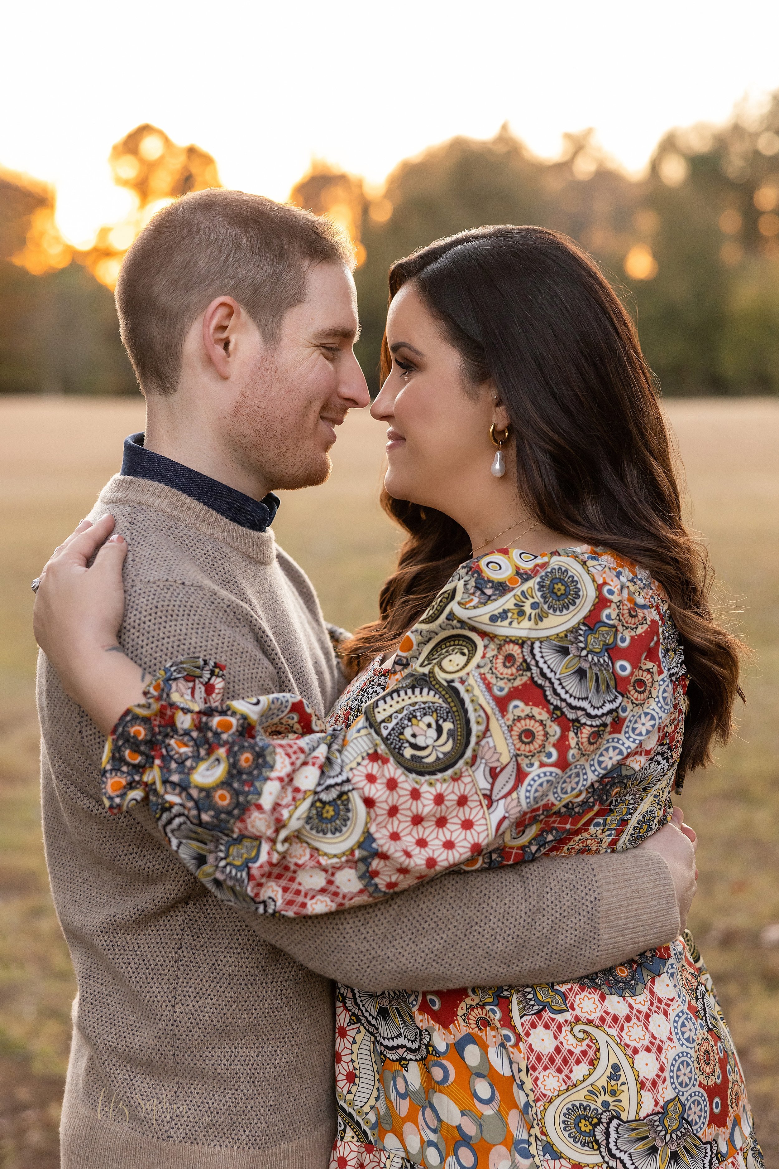  Family portrait of a husband and wife as they hug one another in a park with the sun setting behind them during the fall season in Atlanta, Georgia. 