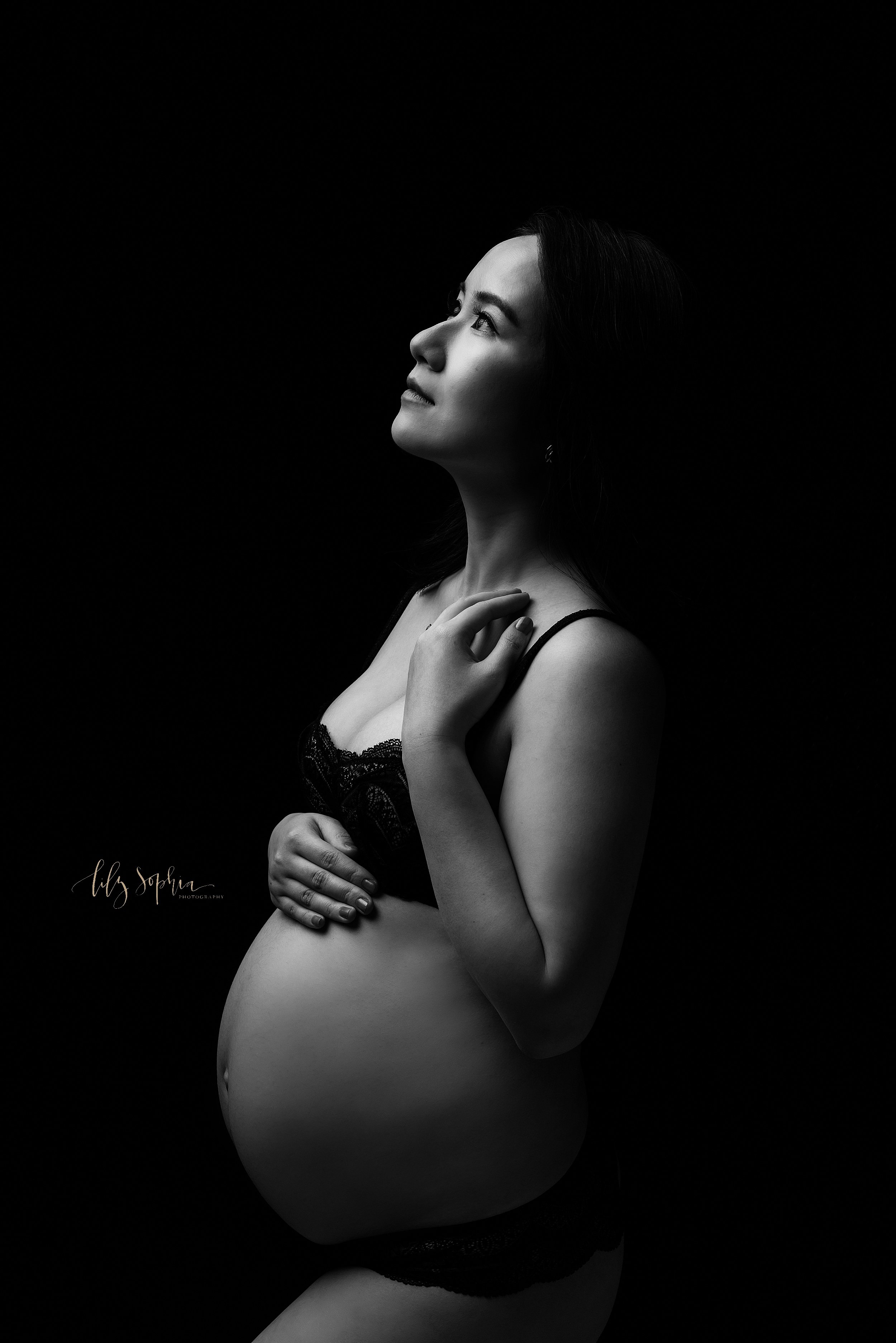  Modern maternity portrait of an Asian mother looking up while standing in underwear with her left hand on top of her belly and her right hand on her right shoulder taken in a studio near Morningside in Atlanta. 