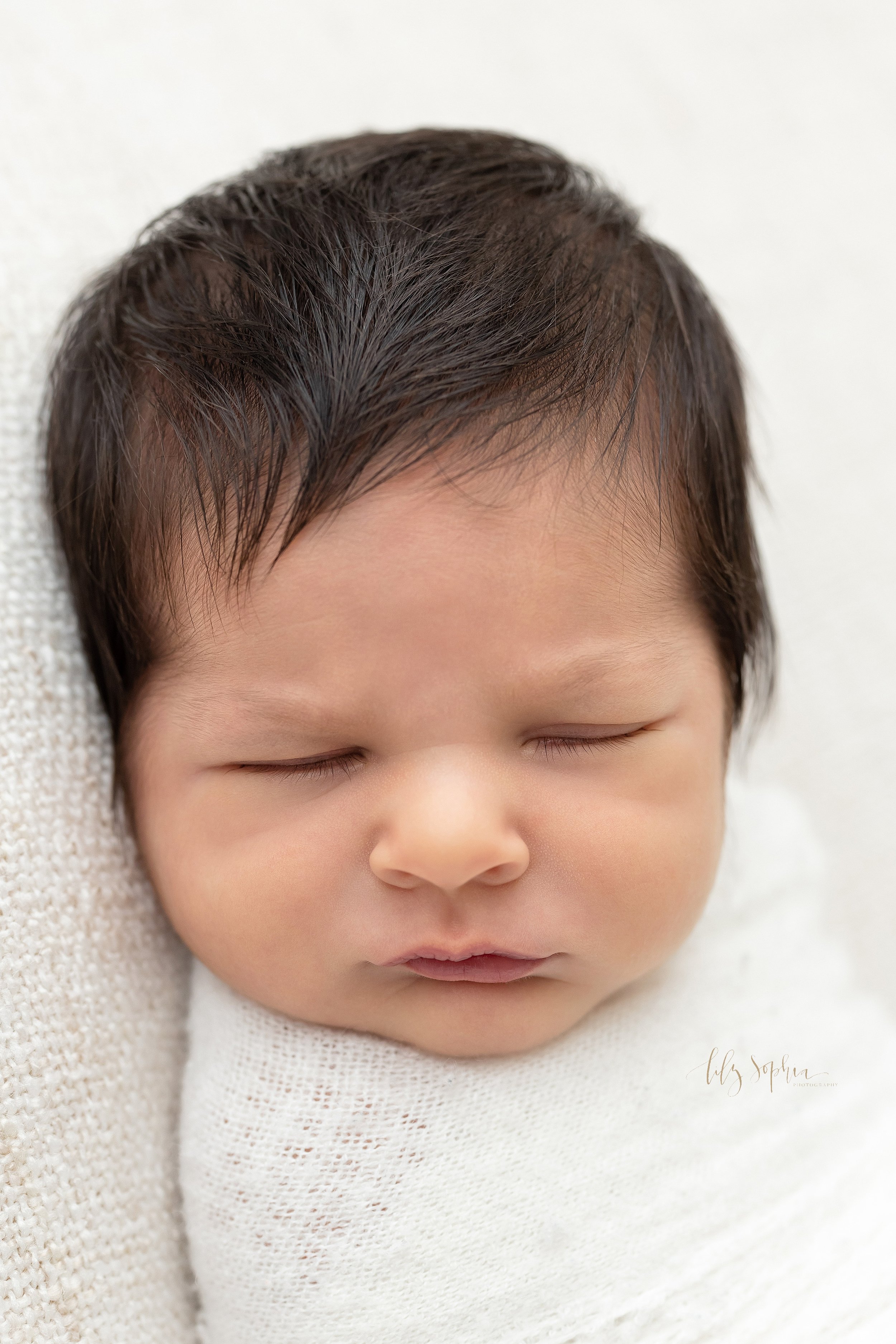  Close-up newborn photo of a peacefully sleeping infant boy to highlight his delicate facial features taken using natural light near Alpharetta in Atlanta in a photography studio. 