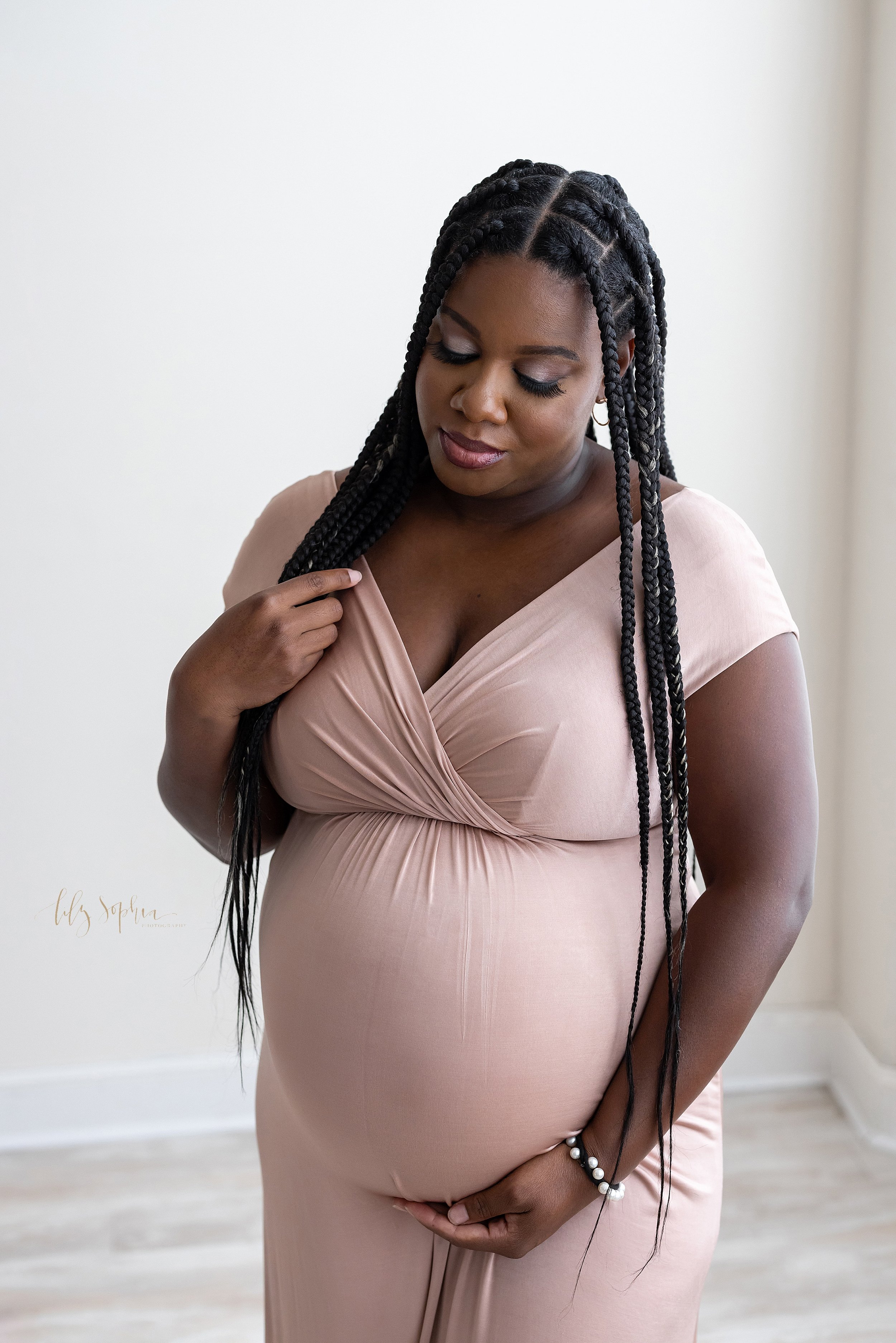  Maternity photoshoot of a black expectant mother as she stands in a studio with her right hand stroking her braids and her left hand holding the base of her belly as she contemplates the wonder of the life growing inside her taken in natural light i