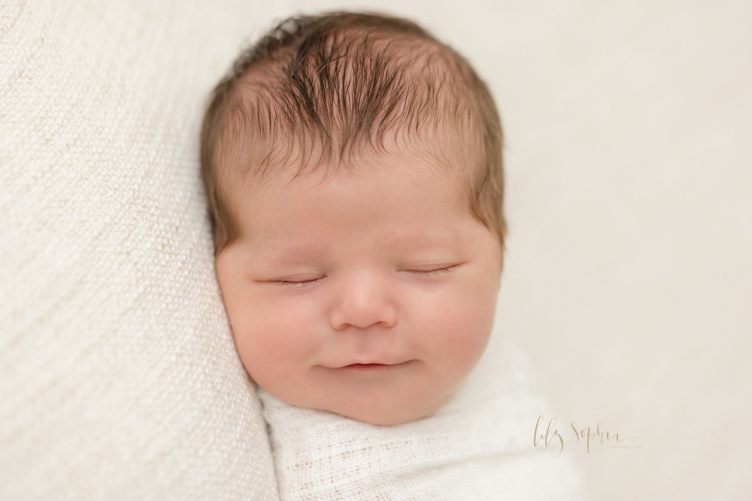  Newborn picture of an infant boy lying on his back with his head turned to his right as he smiles in his sleep taken in natural light in a studio near Vinings in Atlanta, Georgia. 