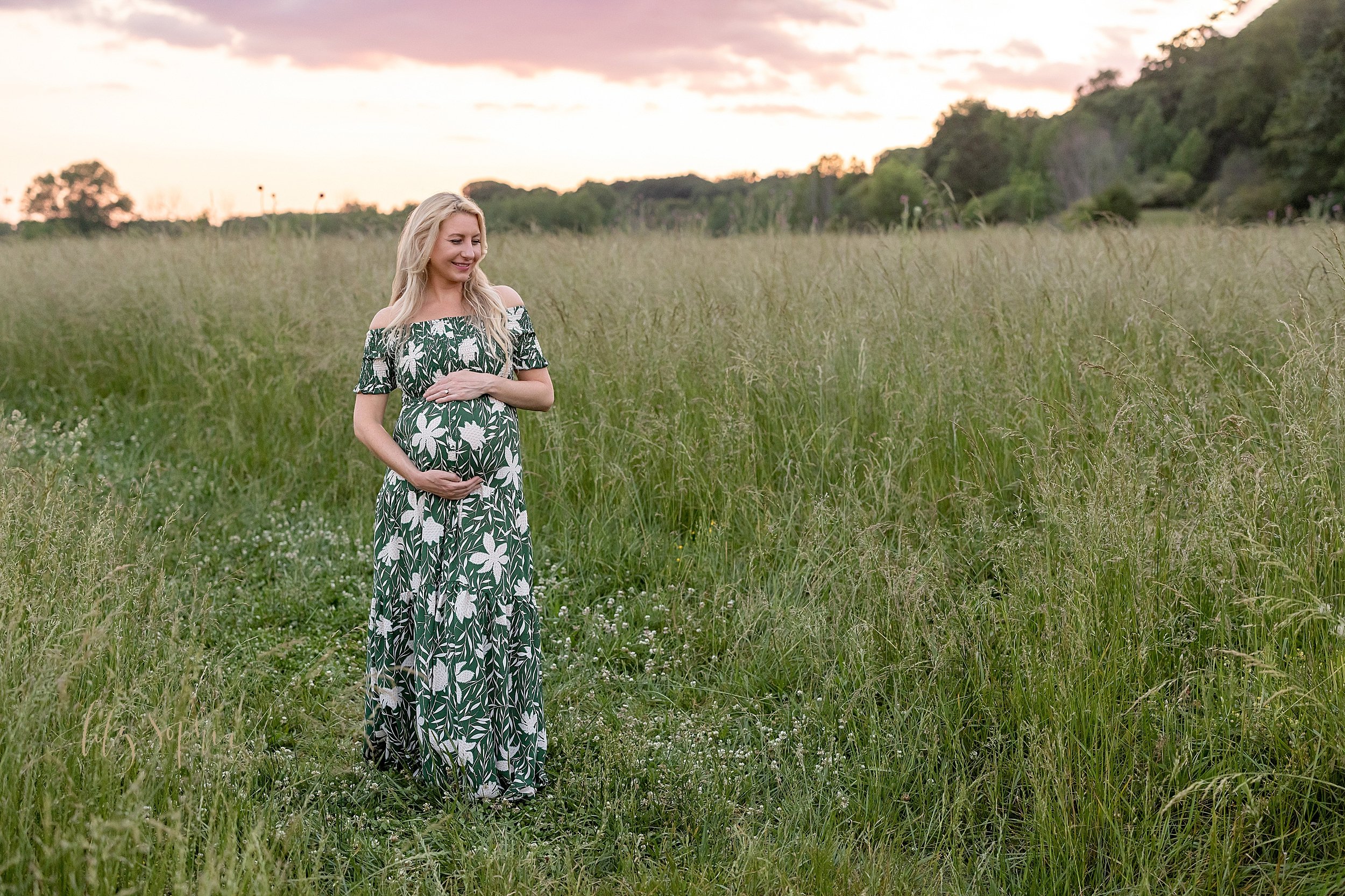  Maternity picture of an expectant mother walking along a field in Atlanta while holding her baby in utero at sunset. 