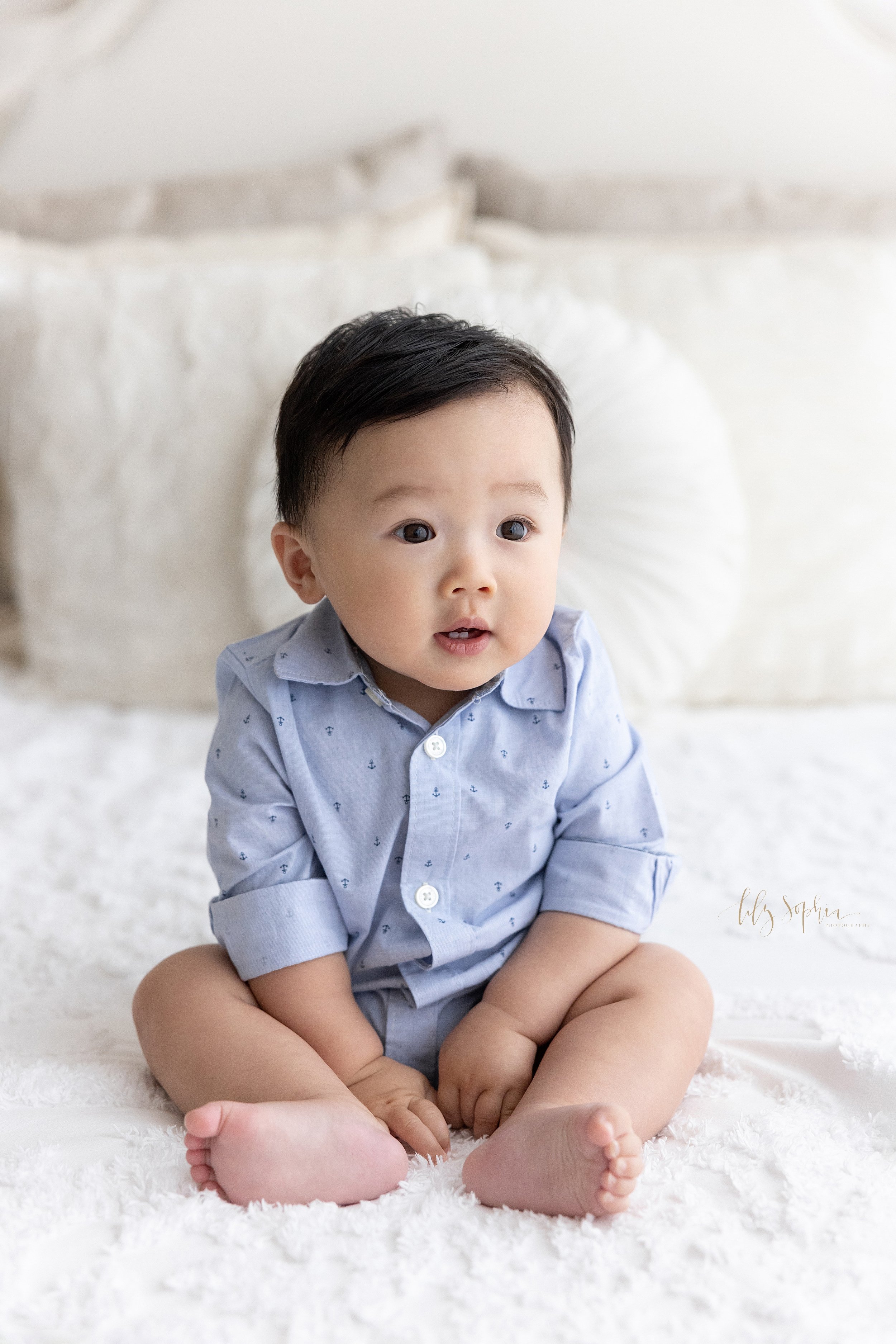  Sitting milestone portrait of an Asian baby boy as he sits on top of a bed next to a window streaming natural light in a studio near Midtown in Atlanta. 