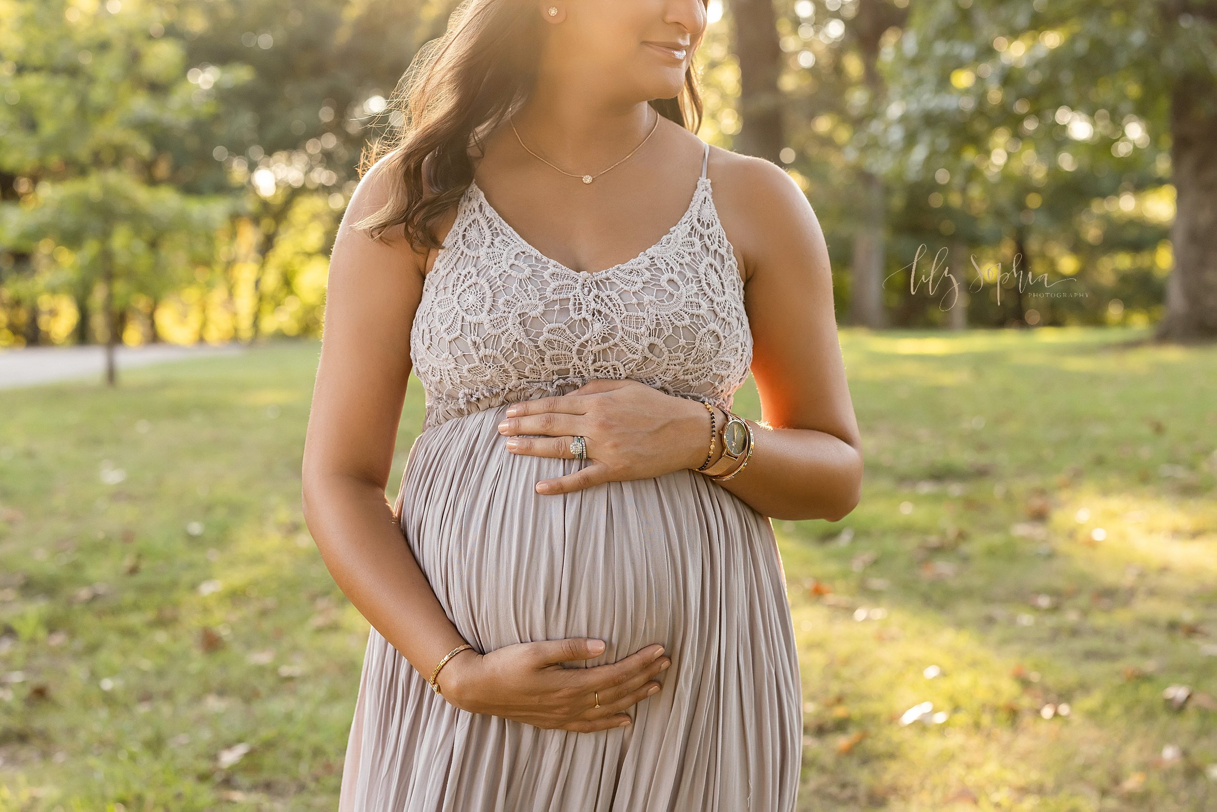  Close-up maternity portrait of a pregnant mother as she stands in a park at sunset framing her belly with her hands taken near Atlanta. 