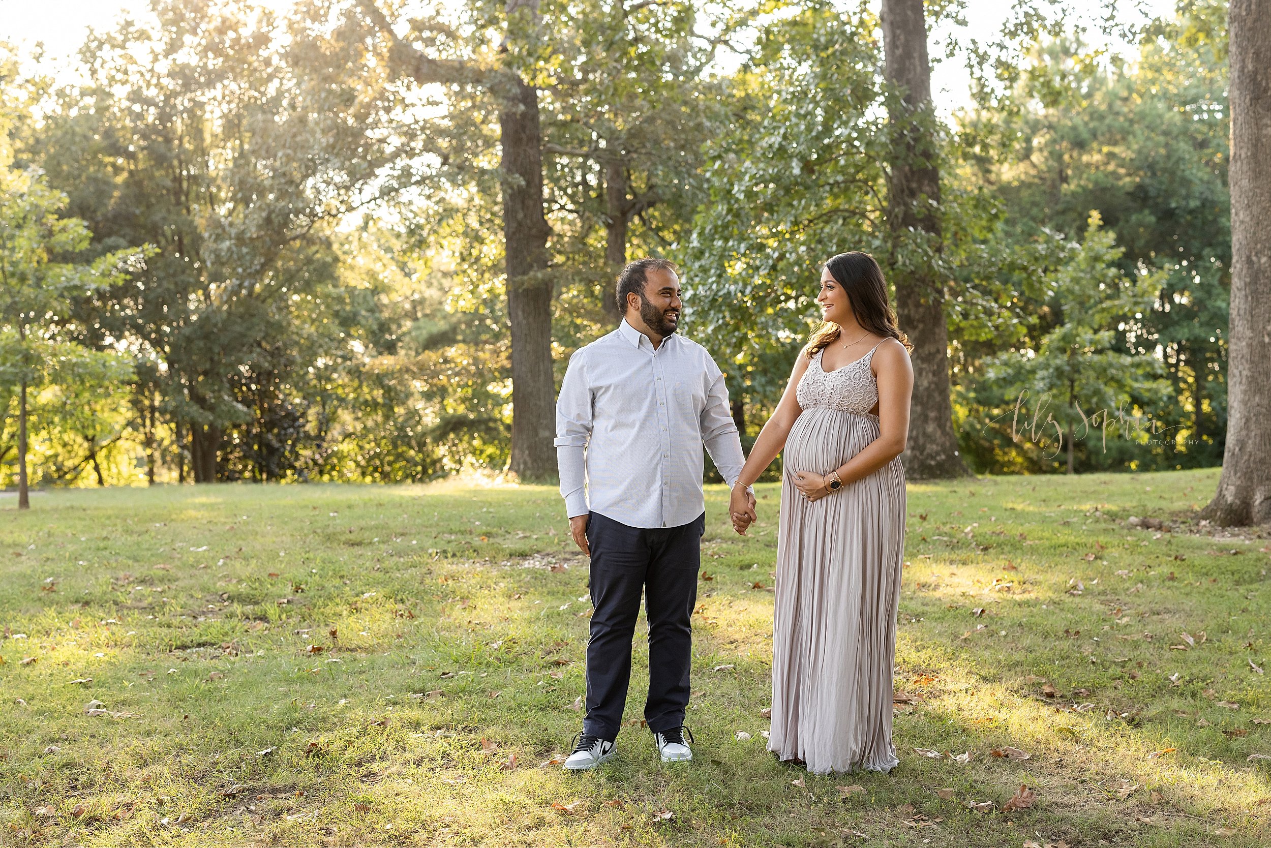  Maternity photo shoot taken in an Atlanta park with the Indian mother to be and father standing and holding hands as they look lovingly at one another at sunset. 