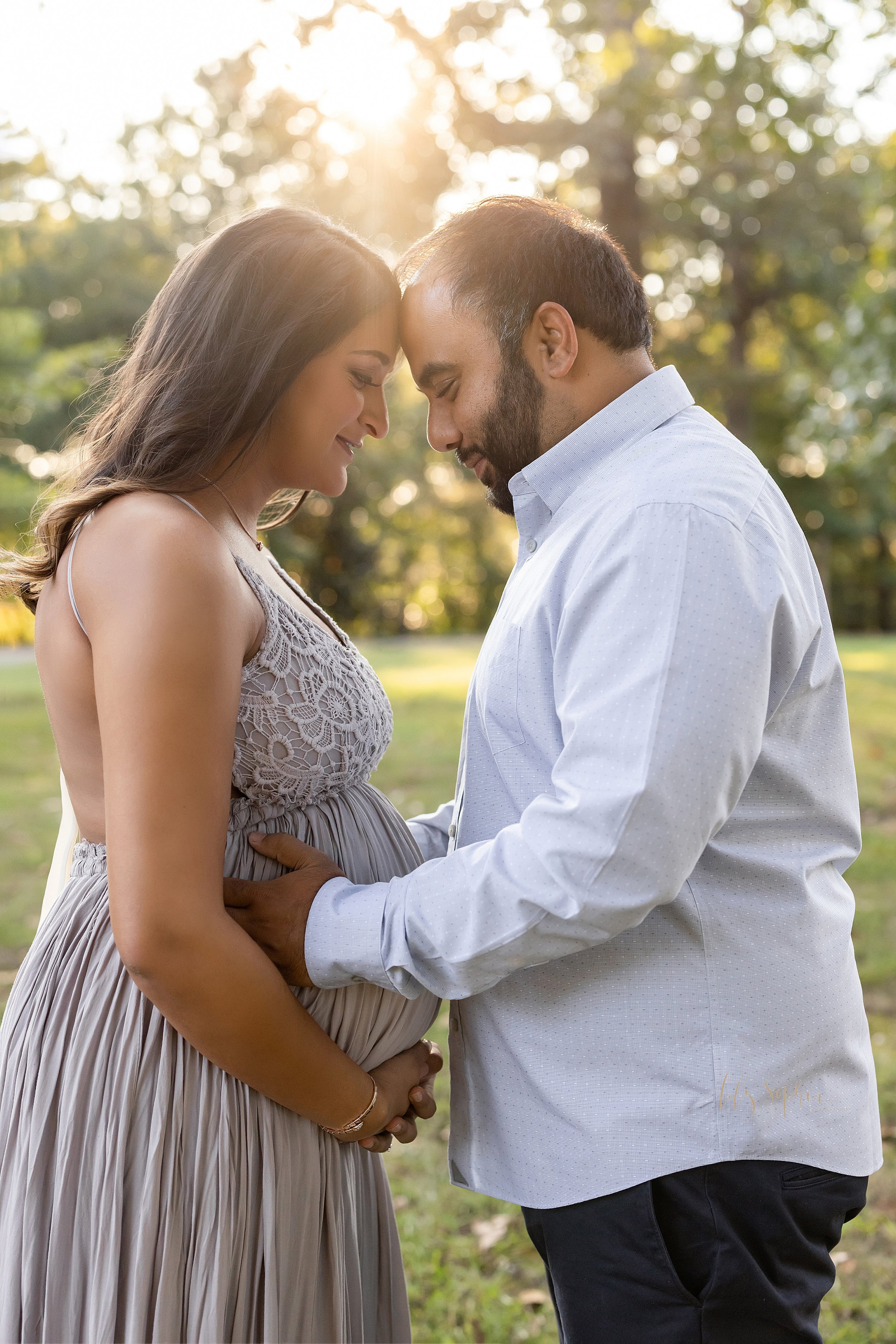 Maternity photo session taken at sunset of a husband and wife facing one another with the pregnant mother holding the base of her belly and the husband holding his wife at her waist as the couple place their foreheads together and contemplate the en