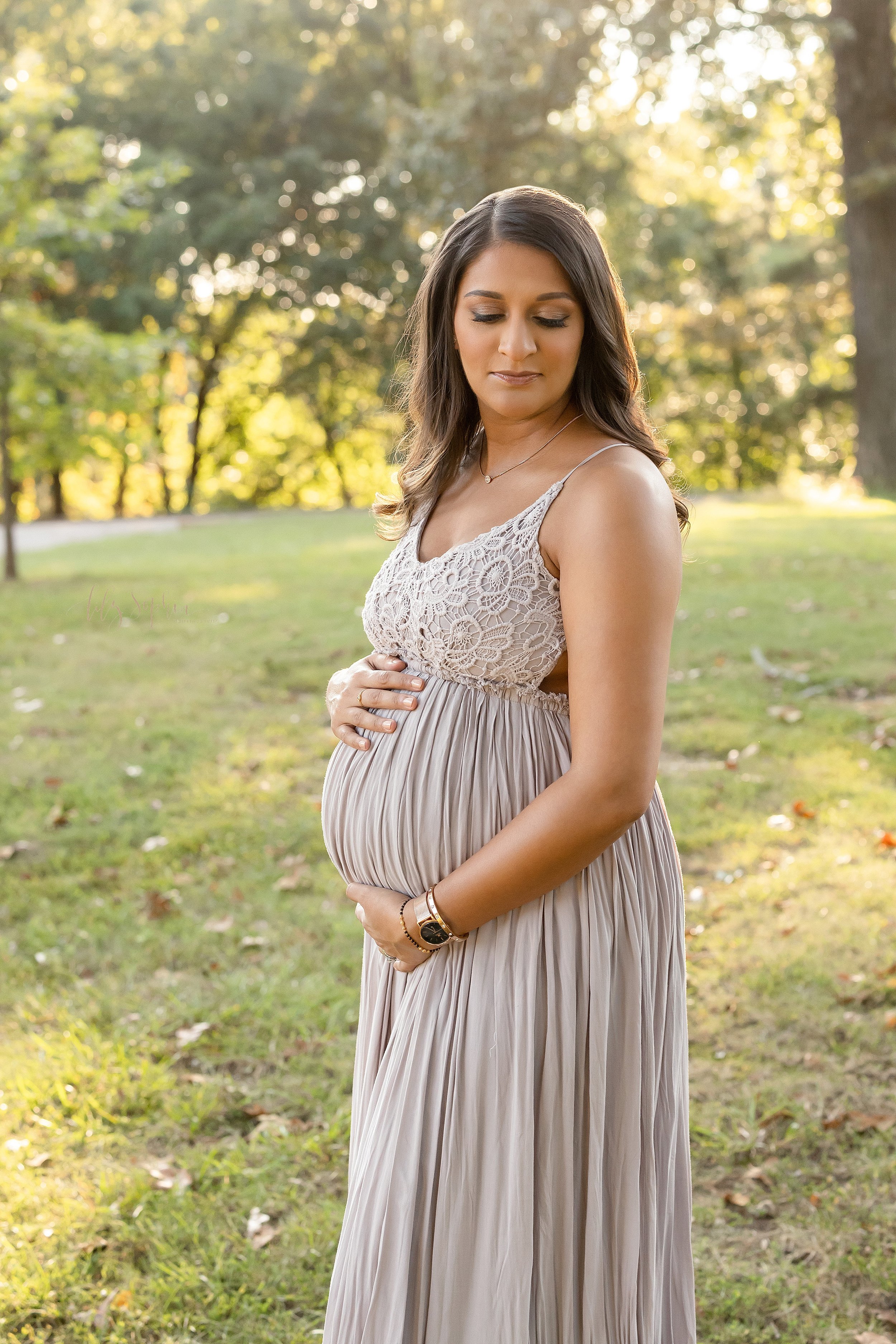  Profile maternity portrait of an Indian mother as she stands at sunset in a park near Atlanta, Georgia and frames her belly with her hands while looking over her left shoulder. 