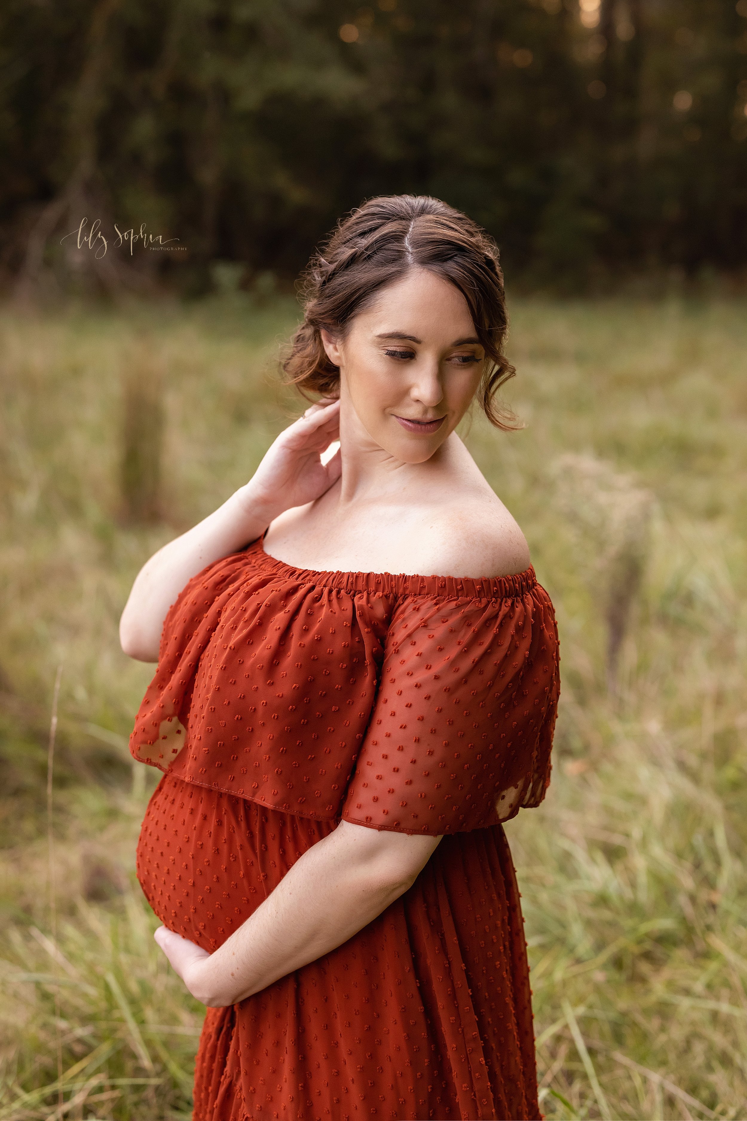  Maternity pictures of pregnant mother as she stands near Atlanta on a mountain with her right hand touching her neck as she looks over her right shoulder while holding the base of her belly with her right hand. 