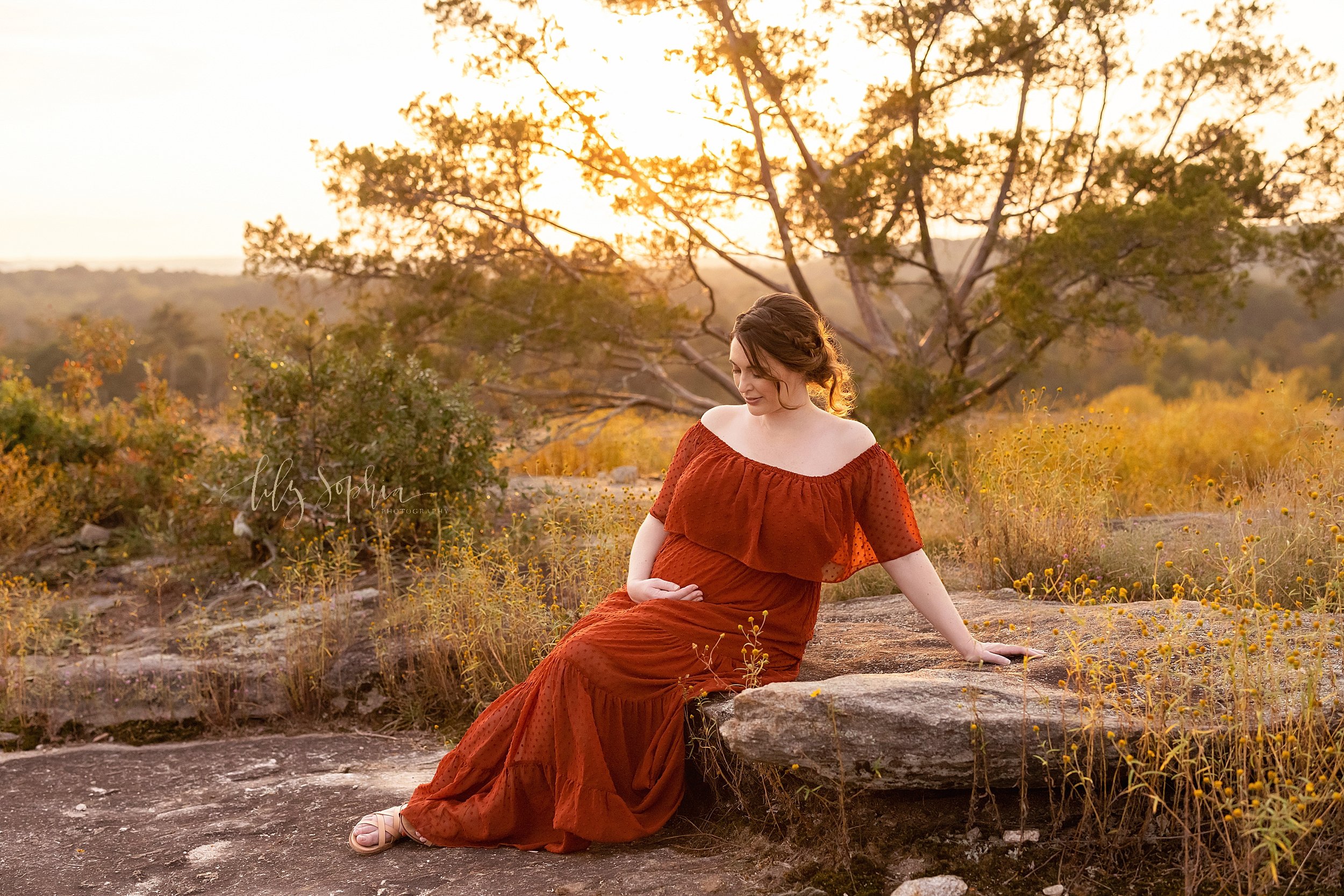  Maternity photo session on a mountain near Atlanta as a pregnant mother sits on a rock at the top of the mountain at sunset. 
