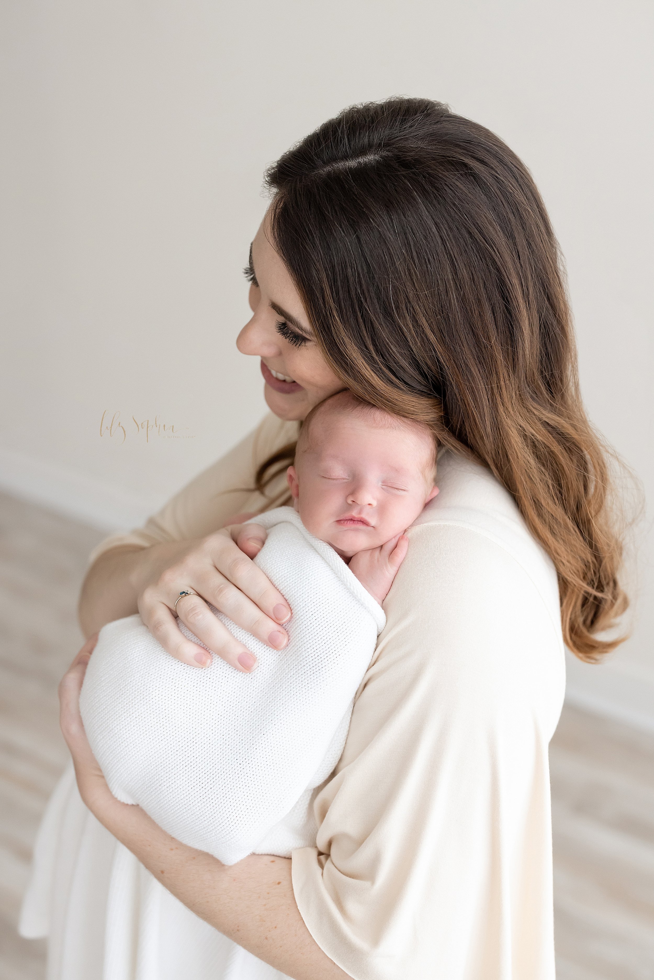  Newborn photo of a mother holding her contented infant boy in her right shoulder as she smiles with pride taken in a studio near Poncey Highlands in Atlanta, Georgia that uses natural light. 