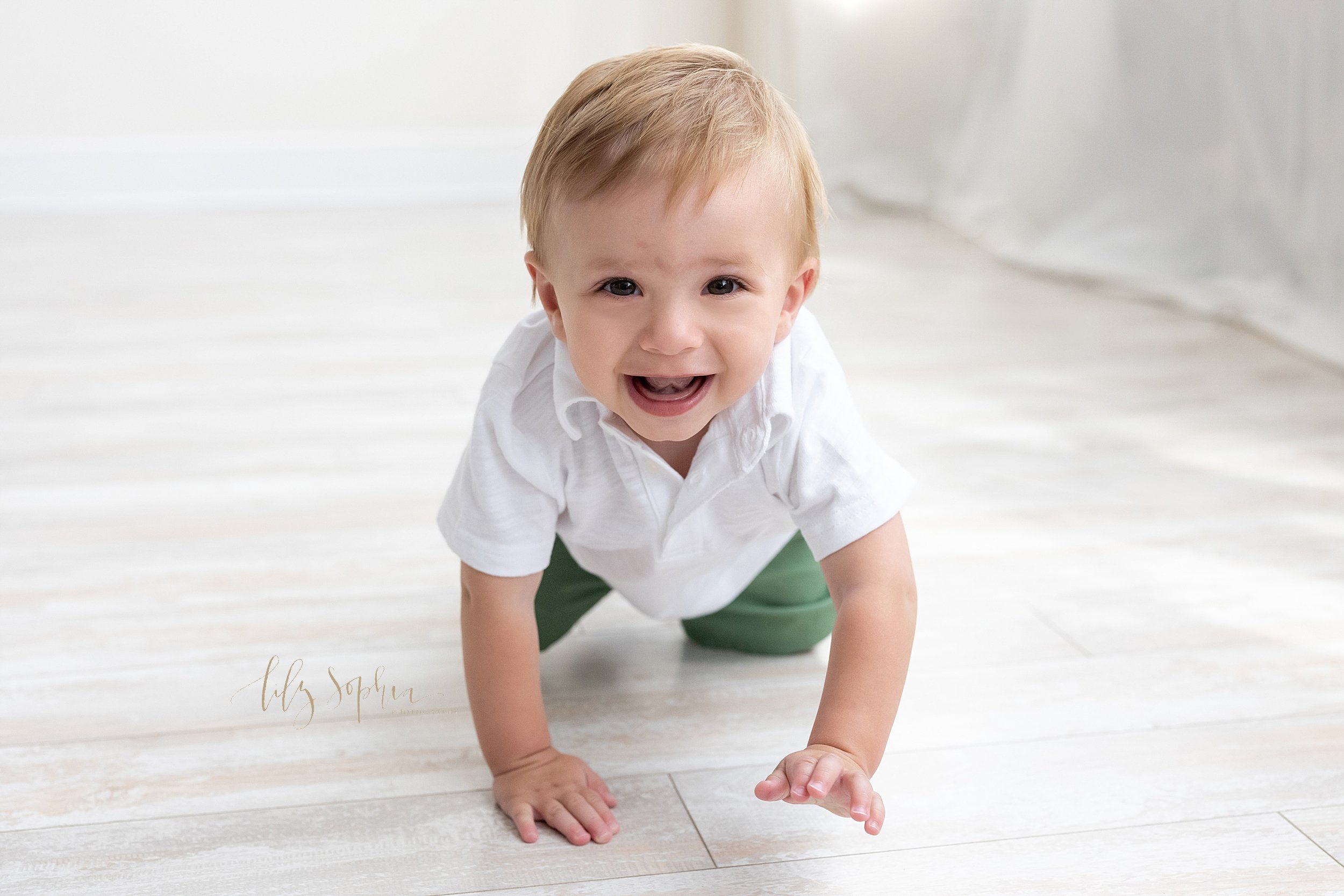  One year little boy crawls across the floor of a natural light studio for his first birthday photo session taken near Old Fourth Ward in Atlanta. 