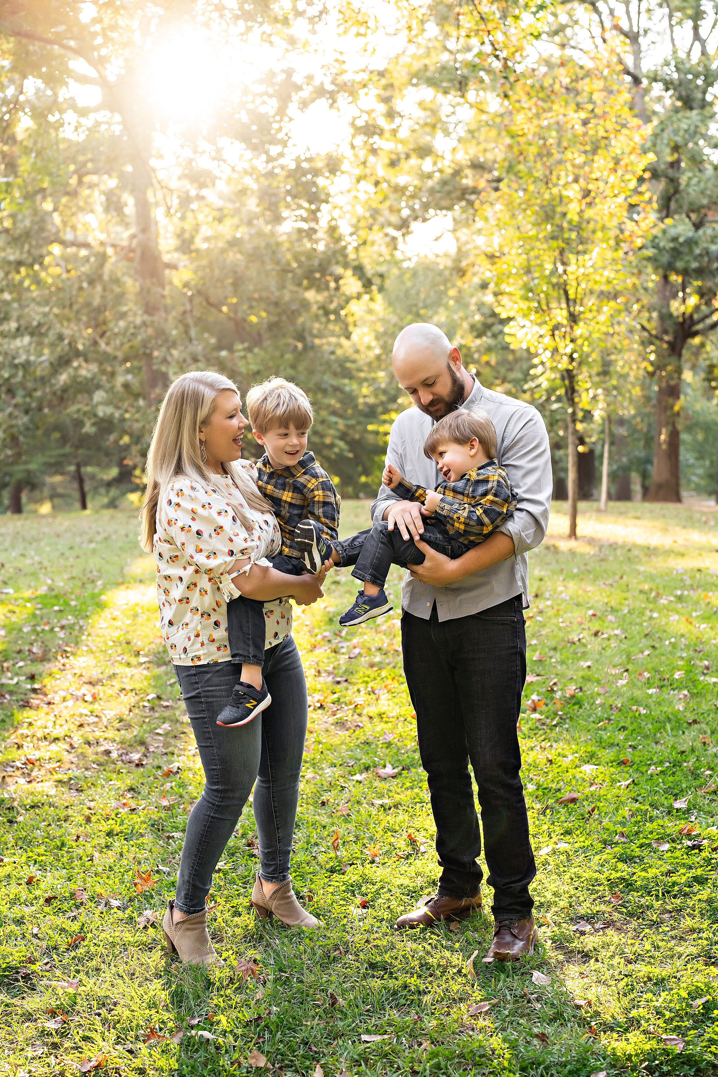  Family portrait with a mother holding her son and facing her toddler son who is being held in his arm by his father as the couple enjoy an autumn day in a park at sunset in Atlanta, Georgia. 