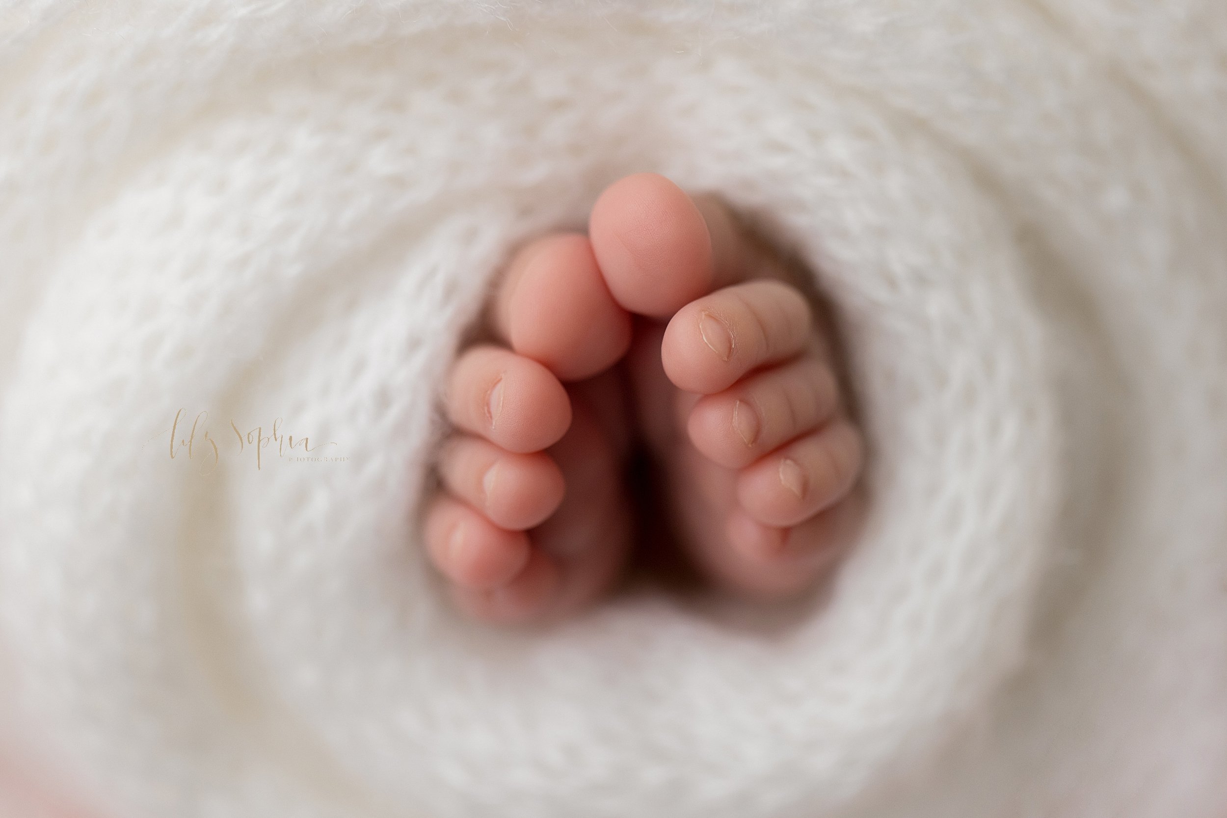  Newborn photo session of the tiny toes of a newborn baby girl as they peek out from a soft white knitted blanket taken in a natural light studio near Midtown in Atlanta. 
