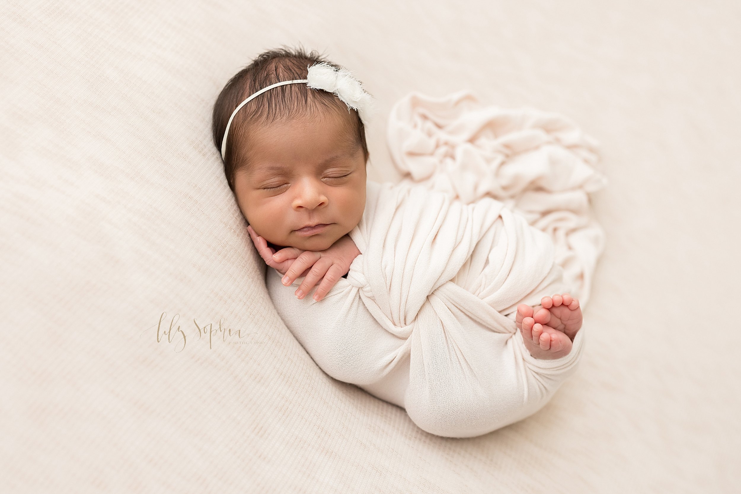  Newborn photo shoot of a peacefully sleeping Indian newborn baby girl wrapped in a stretchy swaddle with her delicate fingers on her cheek and under her chin and her tiny toes peeking out taken using natural light near Alpharetta in Atlanta in a pho