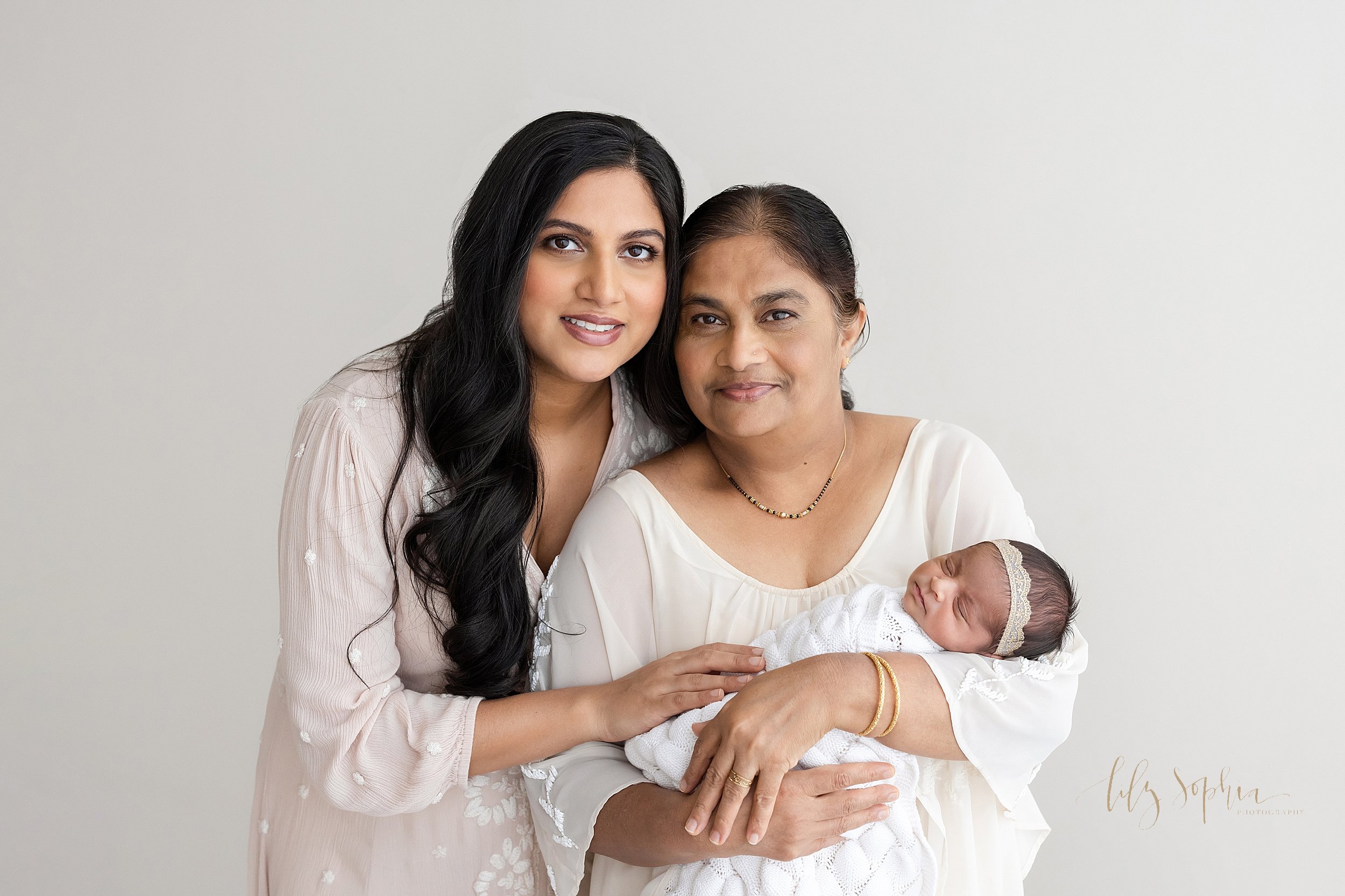  Intergenerational family newborn portrait with mom standing to the right side of her mother as the grandmother cradles her newborn granddaughter in her arms taken using natural light in a studio near Decatur in Atlanta, Georgia. 