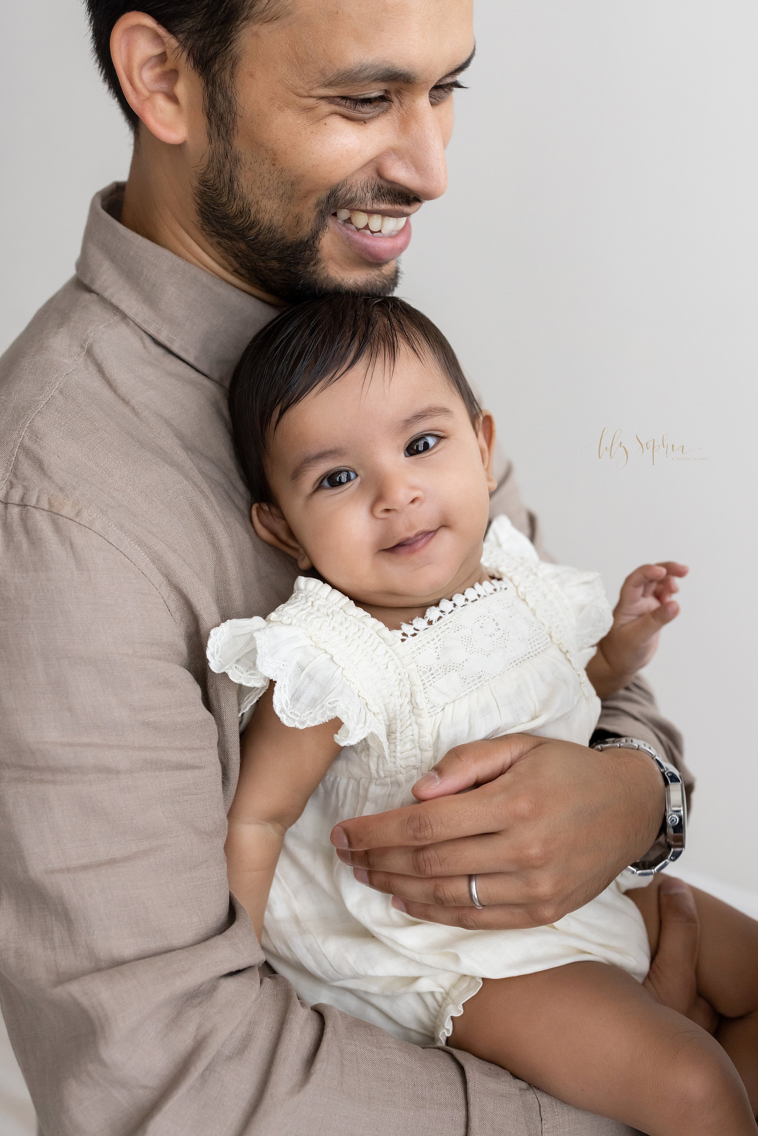  Close-up family portrait of am Indian father holding his contented baby girl in front of him taken in natural light near Old Fourth Ward in Atlanta in a photography studio. 