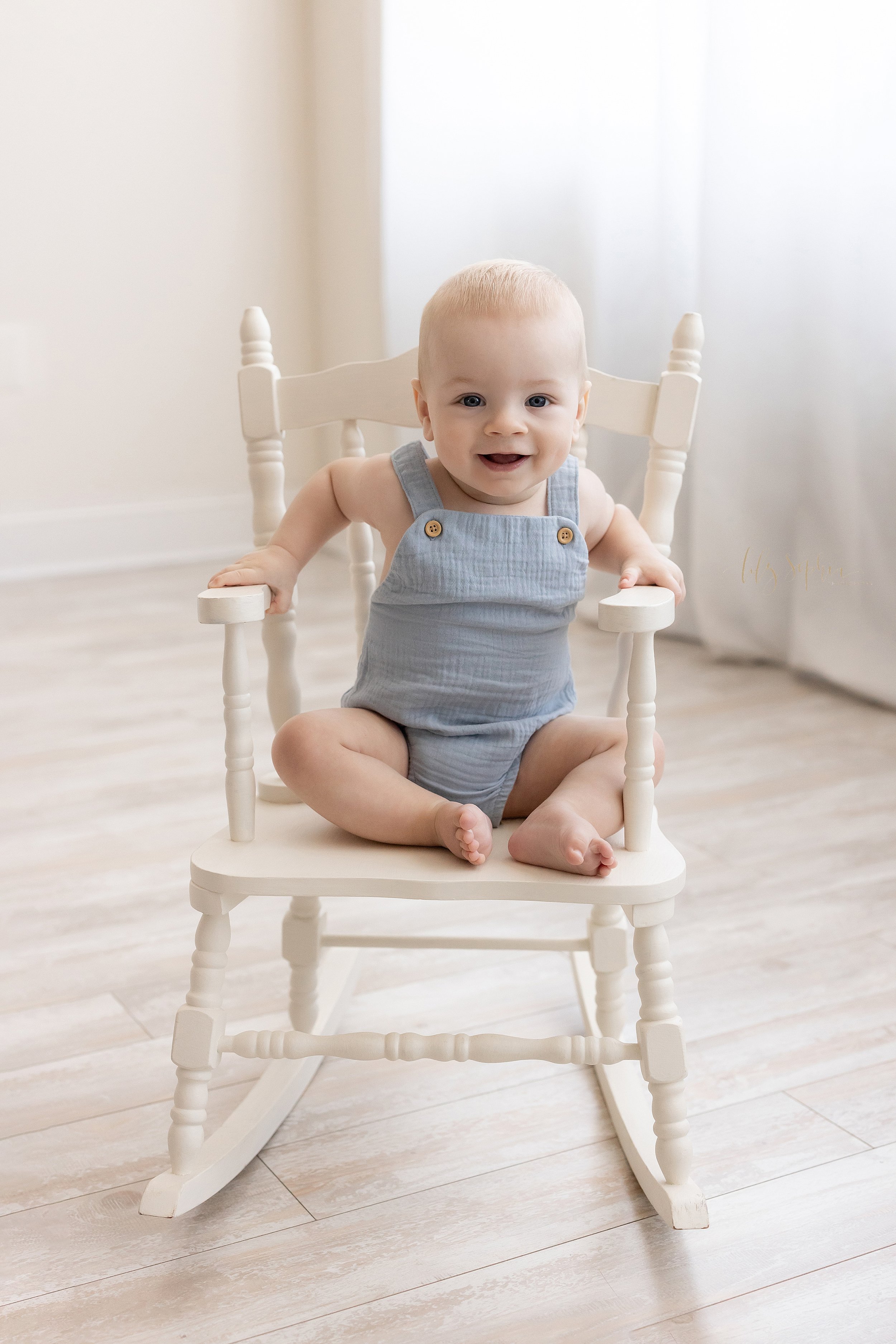  Baby milestone portrait of a baby boy sitting in a rocking chair in front of a window streaming natural light in a studio near Morningside in Atlanta. 