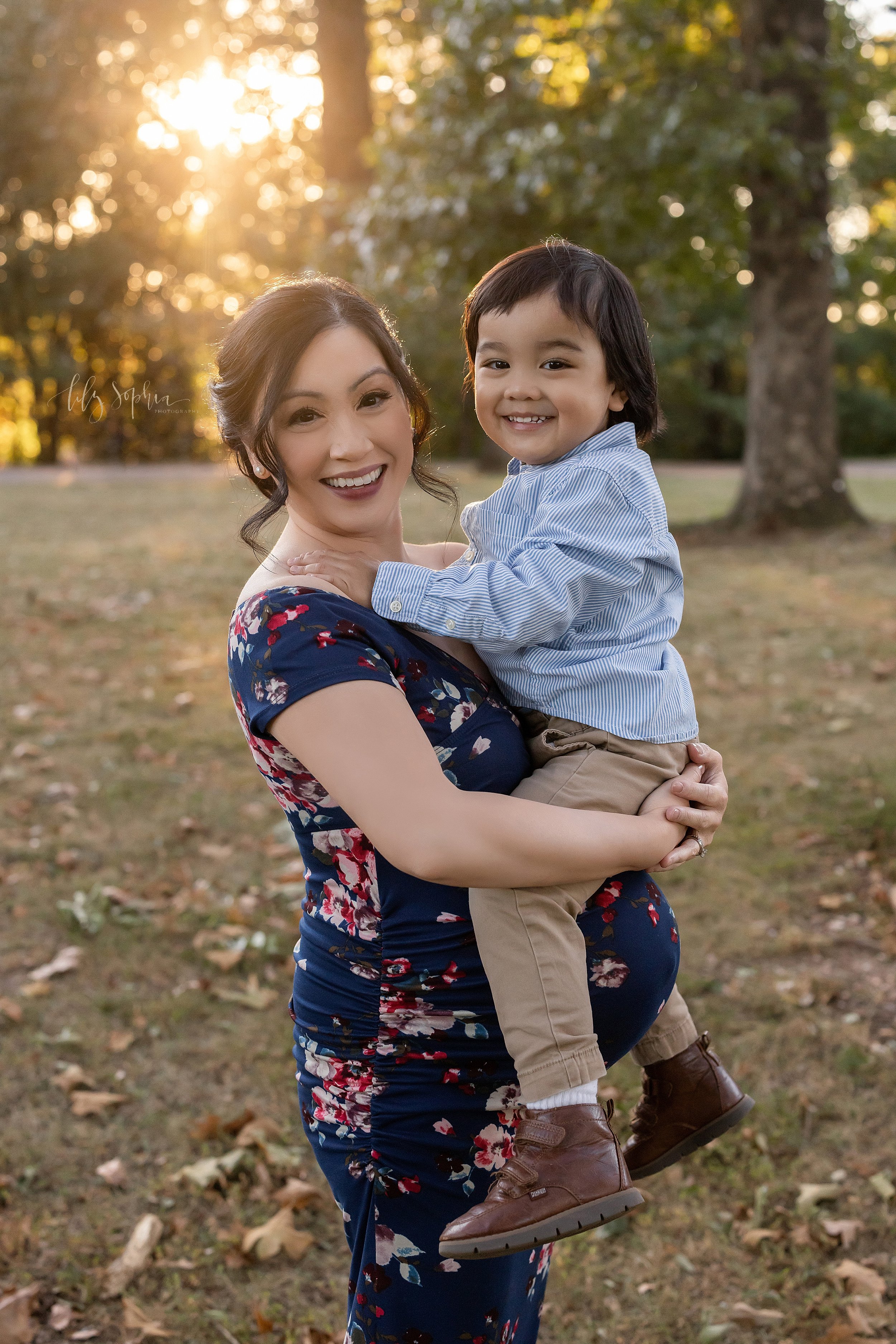  Maternity photo session in an Atlanta park at sunset of an Asian mother holding her young son in her arms. 