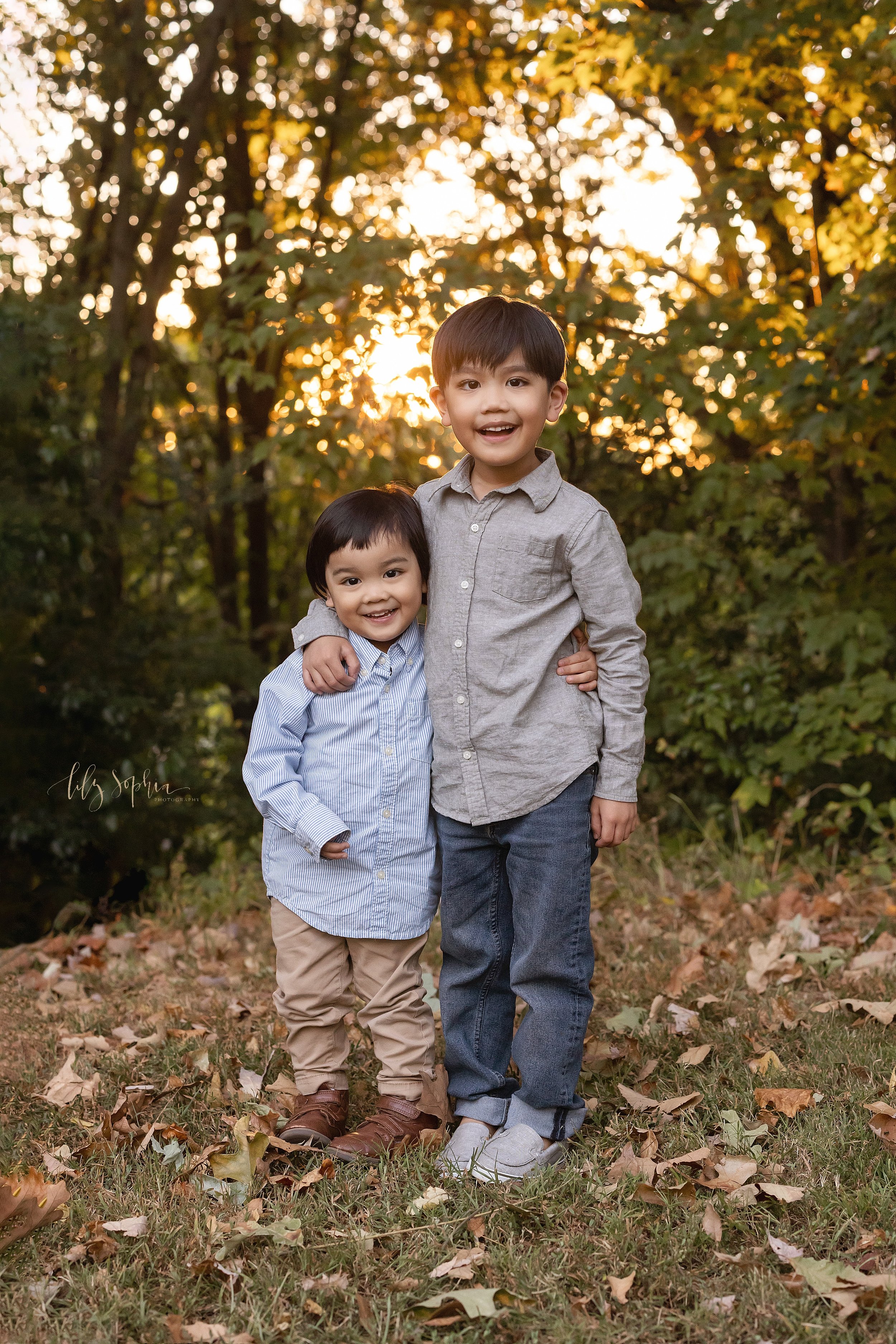  Family photo of Asian brothers as the older brother wraps his arm around the shoulder of the younger bother taken in an Atlanta park at sunset. 