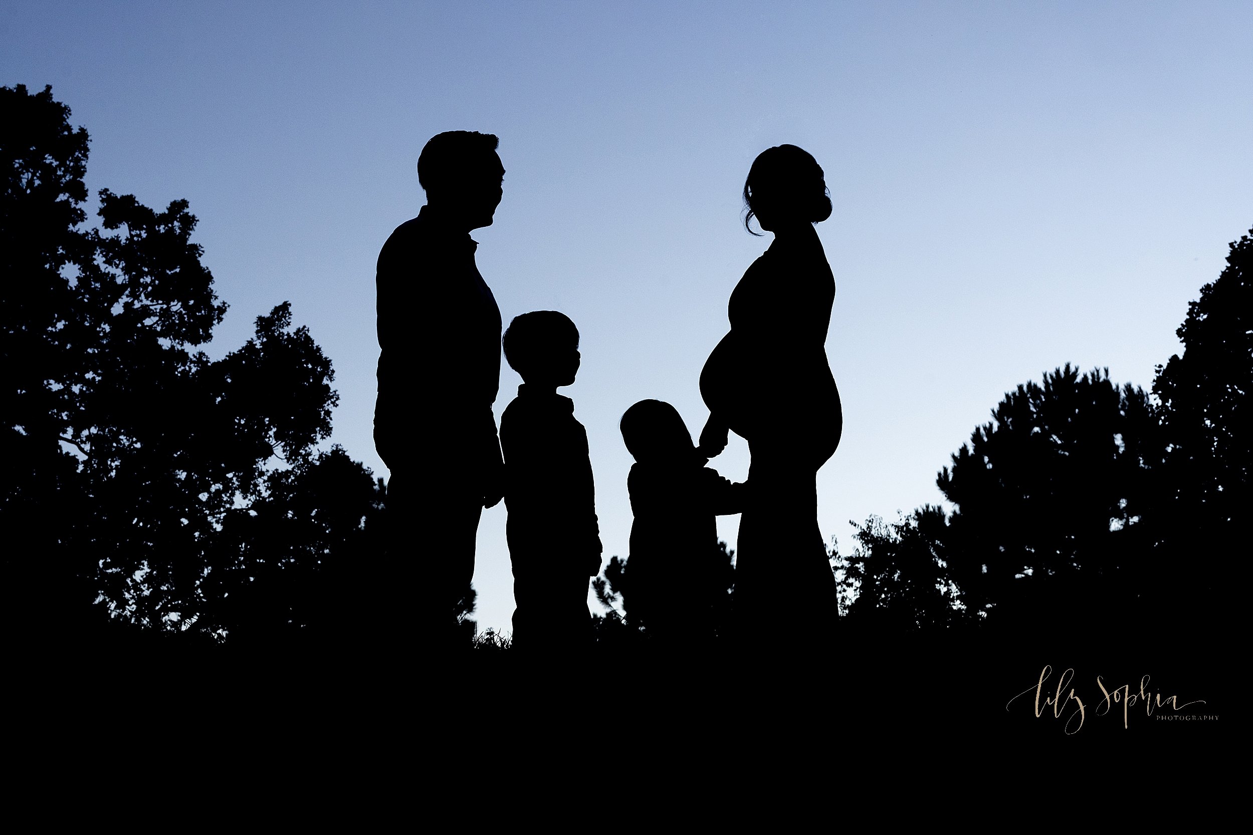  Maternity family silhouetted photo as they stand atop a hill at sunset in a park in Atlanta, Georgia. 