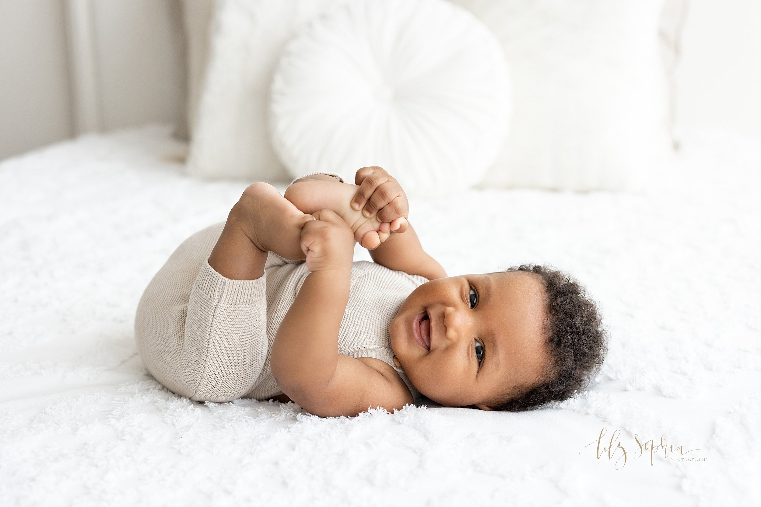  Baby photo of an African-American baby boy lying on his back holding his toes and smiling taken in a natural light studio near Morningside in Atlanta, Georgia. 