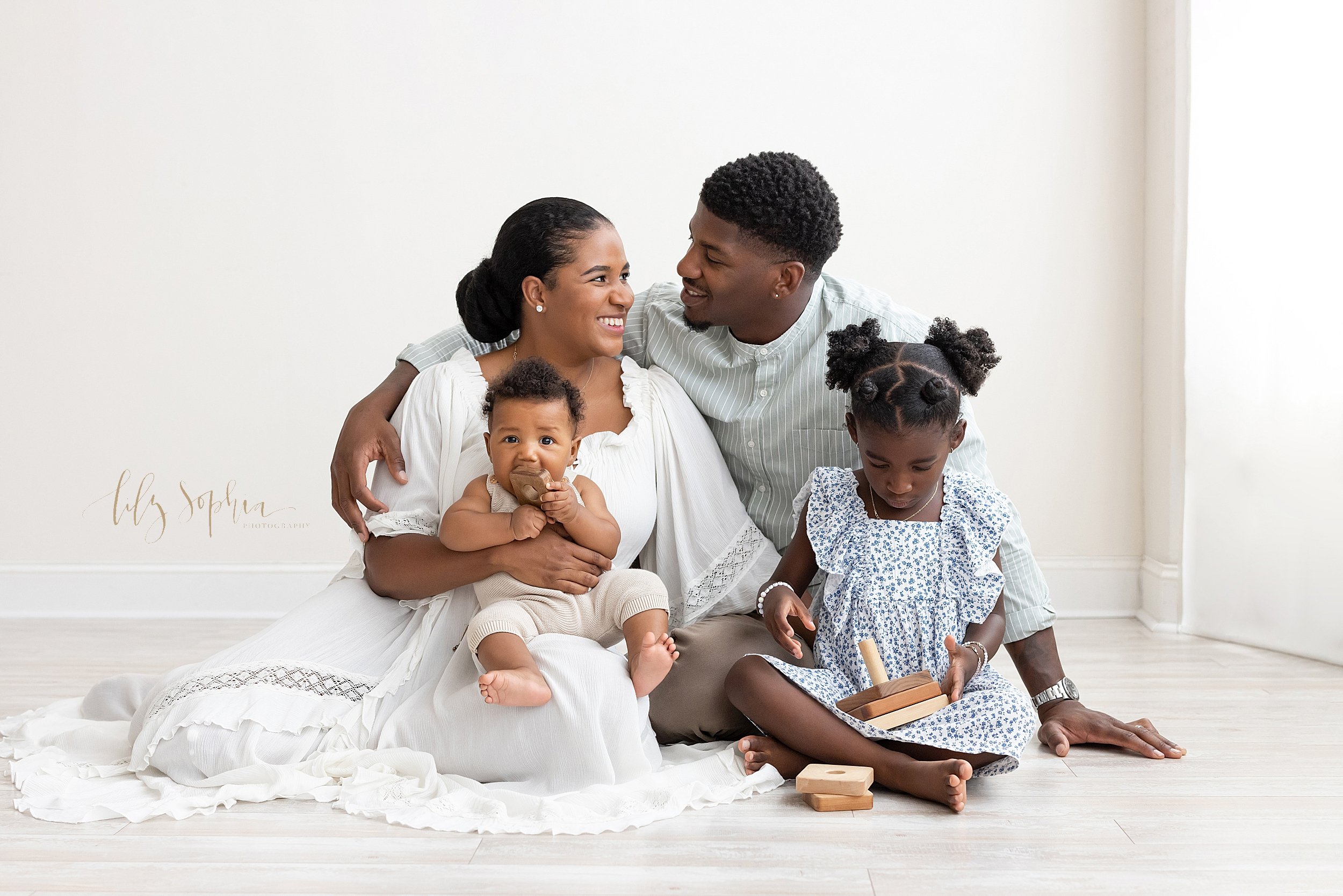  Family photos of an African-American family with the mom holding her baby son on her lap as he chews on a wooden toy, her husband sits next to her with his arm around her shoulder, and her young daughter sits in front of her father playing with a wo
