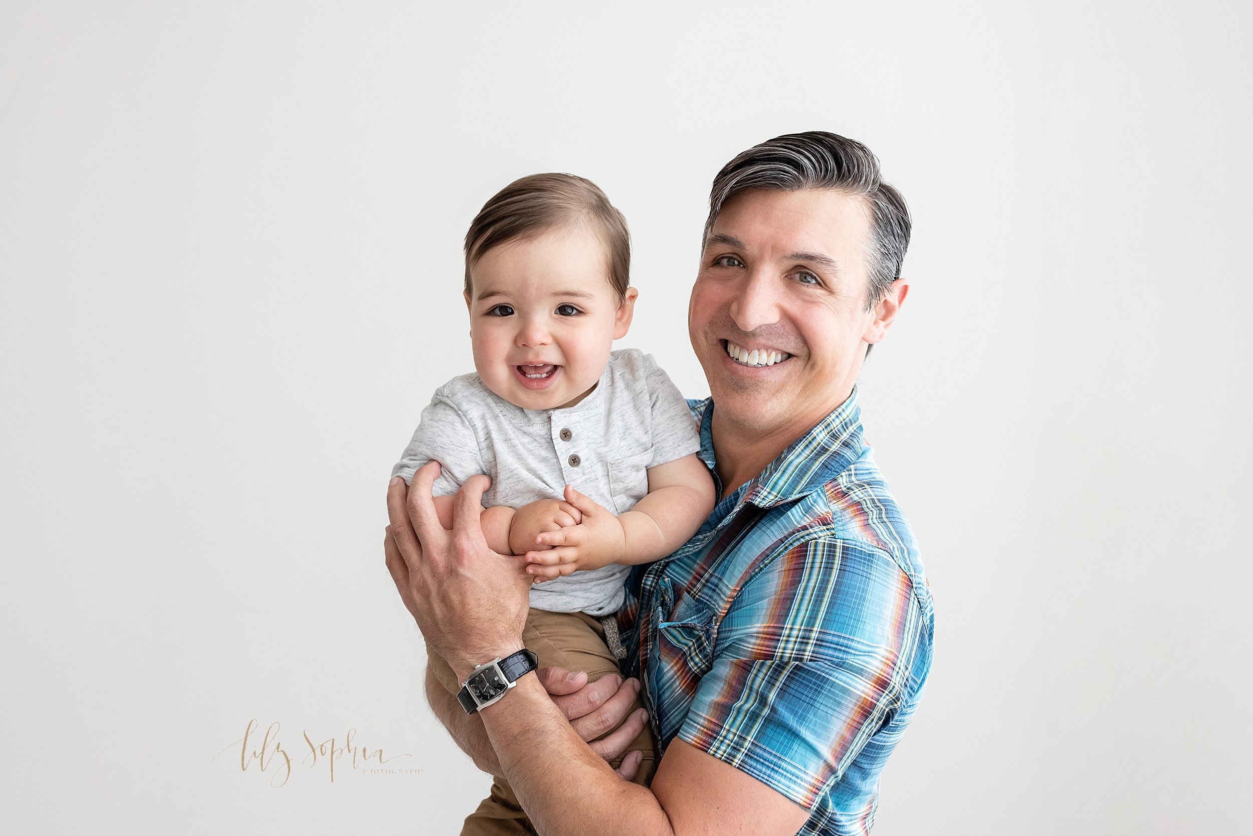  First birthday family photo shoot with dad holding his one year old son in his arms taken in a studio near Morningside in Atlanta that uses natural light. 