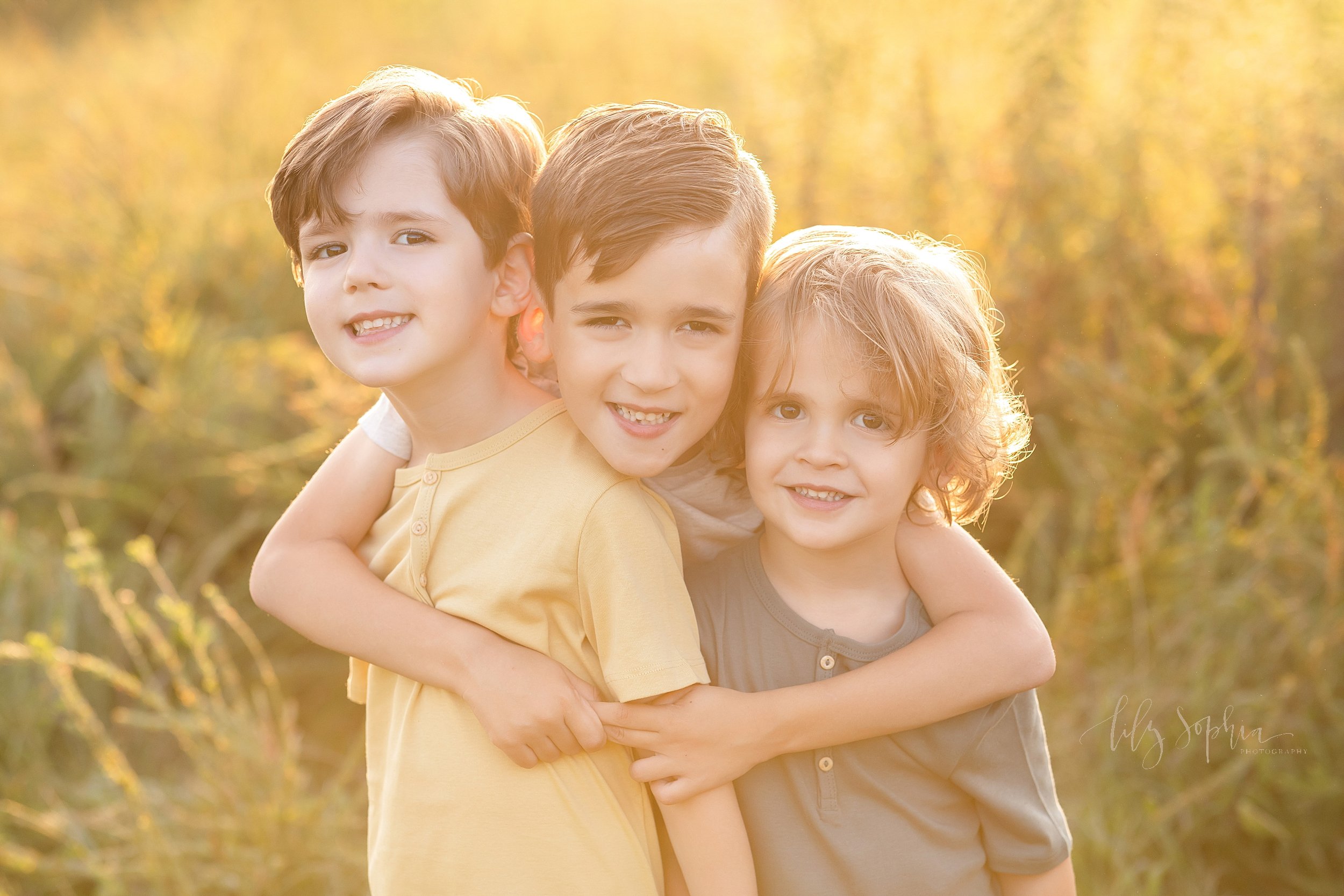  Family photo session with three brothers taken in an Atlanta field at sunset as the eldest brother wraps his arms around his younger brothers. 