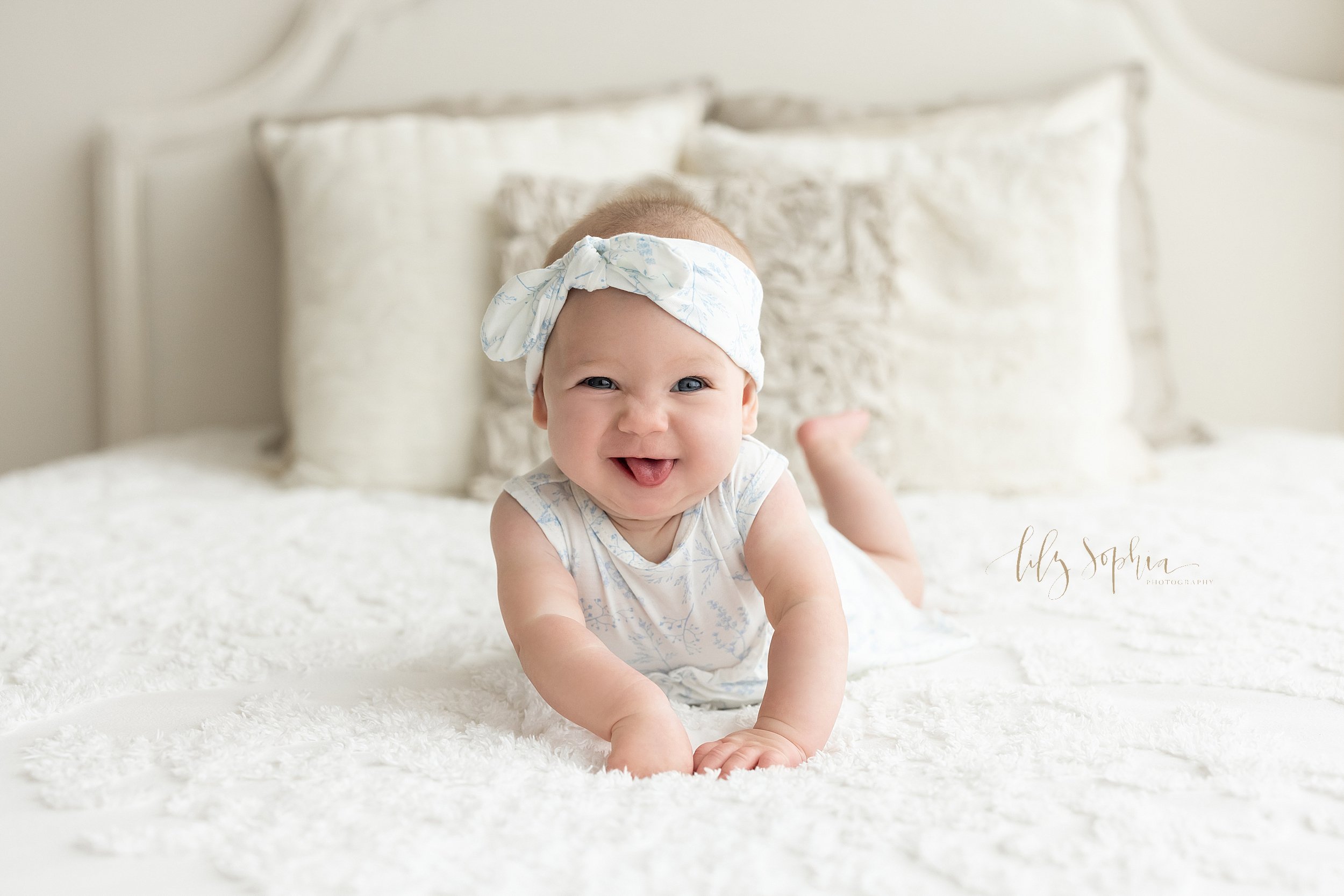  Baby photo of a baby girl wearing a headband bow on her head as she pushes herself us while lying on her stomach on a bed in a natural light studio near Buckhead in Atlanta. 
