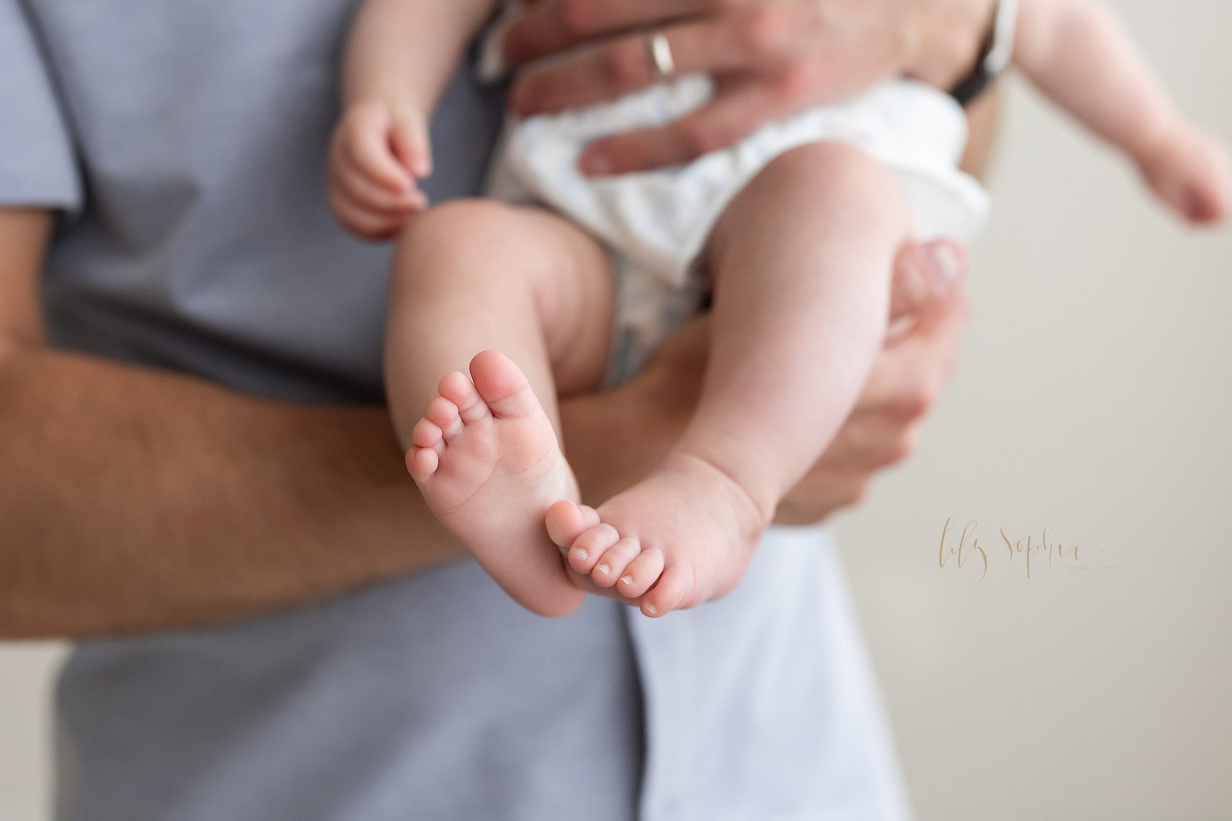  Close-up baby picture of a baby girl’s toes and feet as she is held in a studio near Old Fourth Ward in Atlanta by her father in natural light. 
