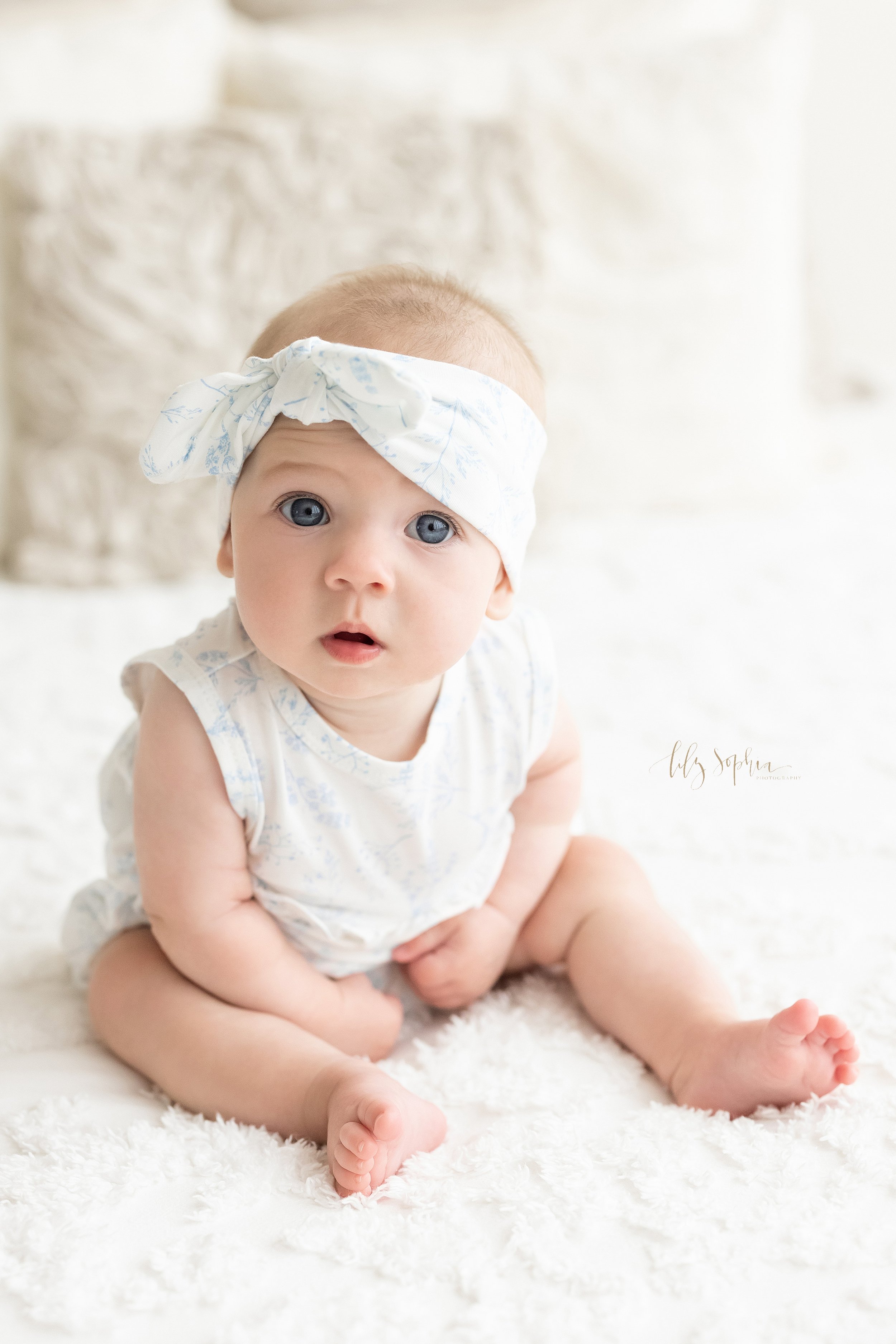  Baby photo session of a baby girl as she sits on top of a bed in front of a window streaming natural light in a studio near Morningside in Atlanta, Georgia. 