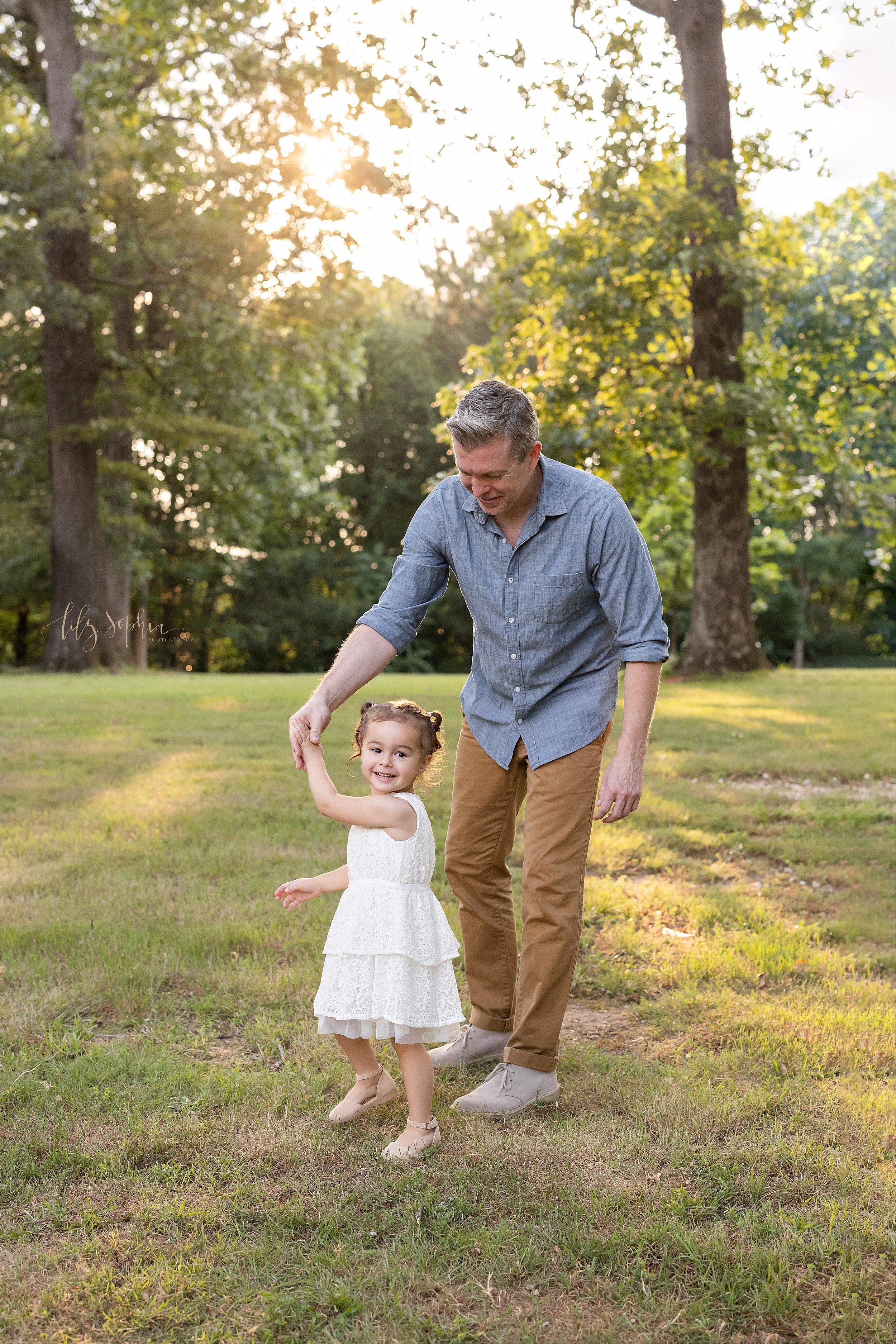  Family portrait of a young daughter dancing with her father at sunset in an Atlanta park. 