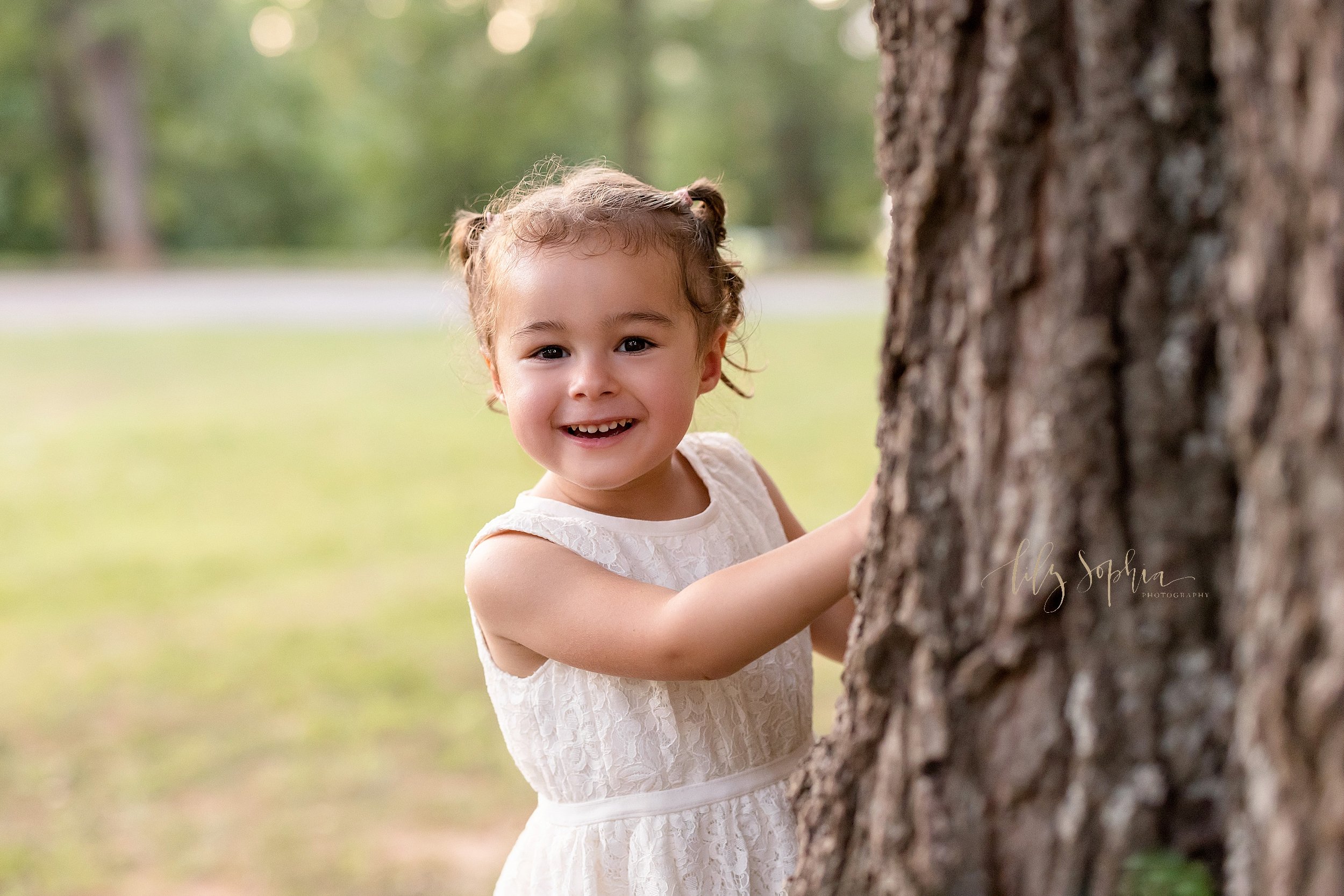  Family photo of a young girl peeking from behind a tree in a park near Atlanta at sunset. 