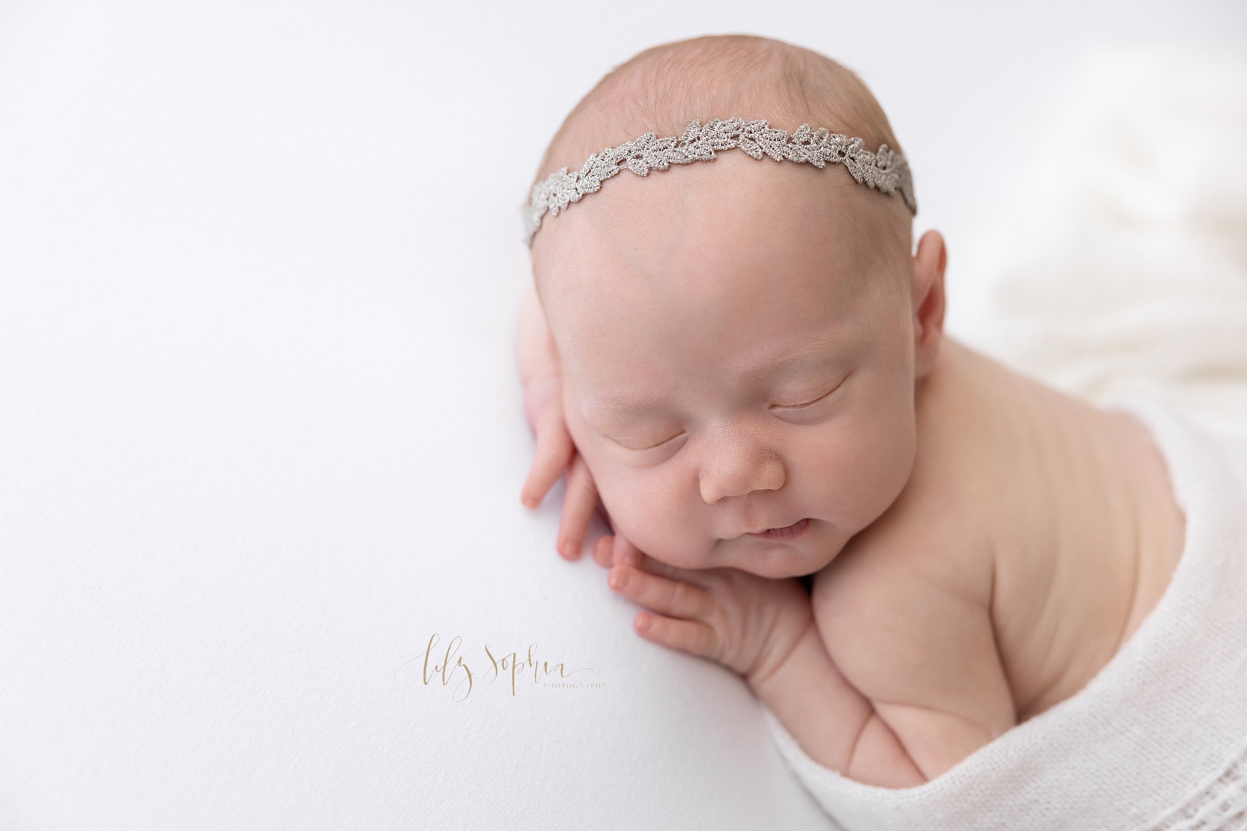  Close-up newborn portrait of a sleeping newborn baby girl lying on her stomach with her hands under her cheek accenting the fat rolls on her arm and back and the delicate features of her face taken in a studio near Oakhurst in Atlanta that uses natu