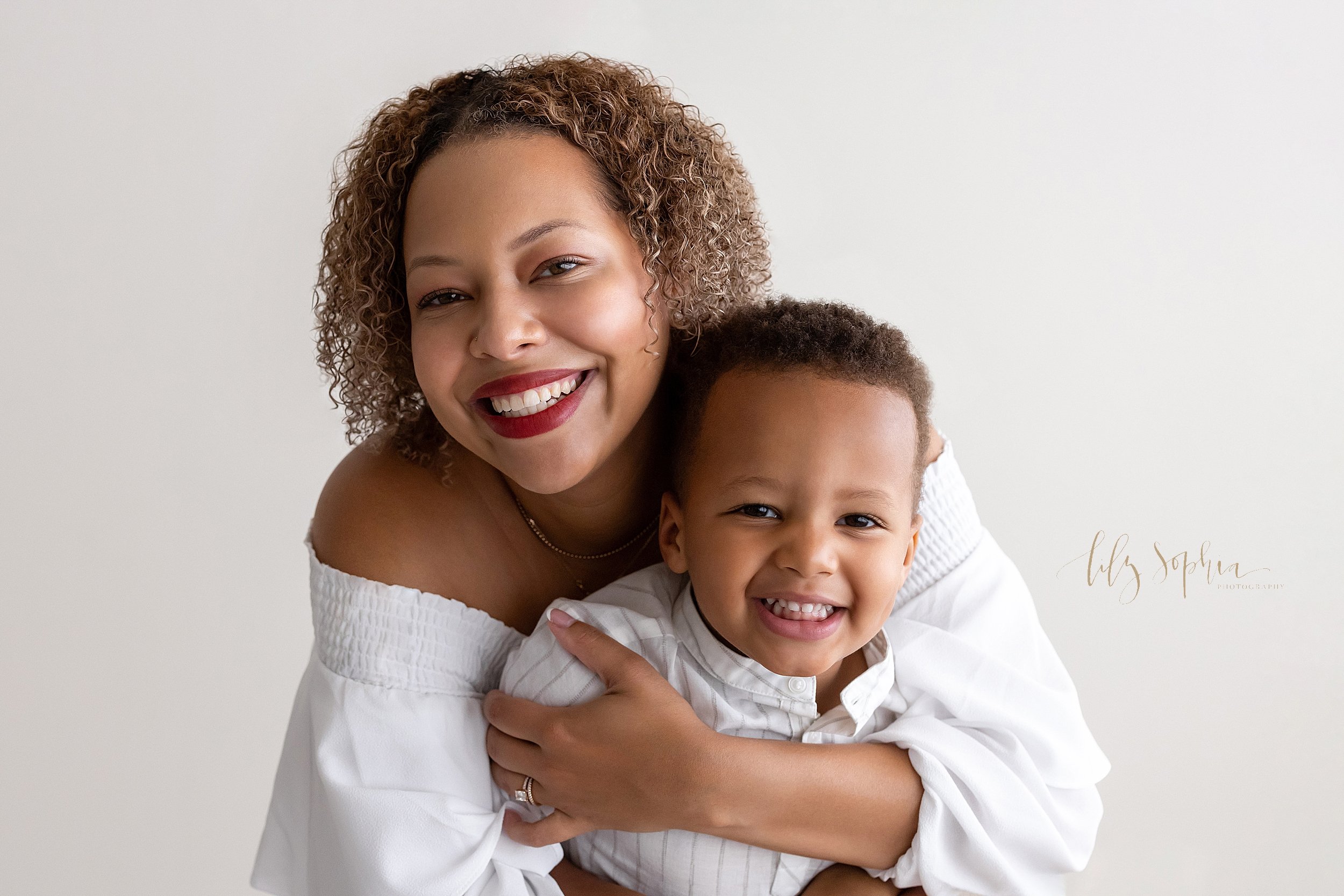  Family photo session in a natural light studio of a mother wrapping her arms around her son who is standing in front of her taken near Old Fourth Ward in Atlanta. 